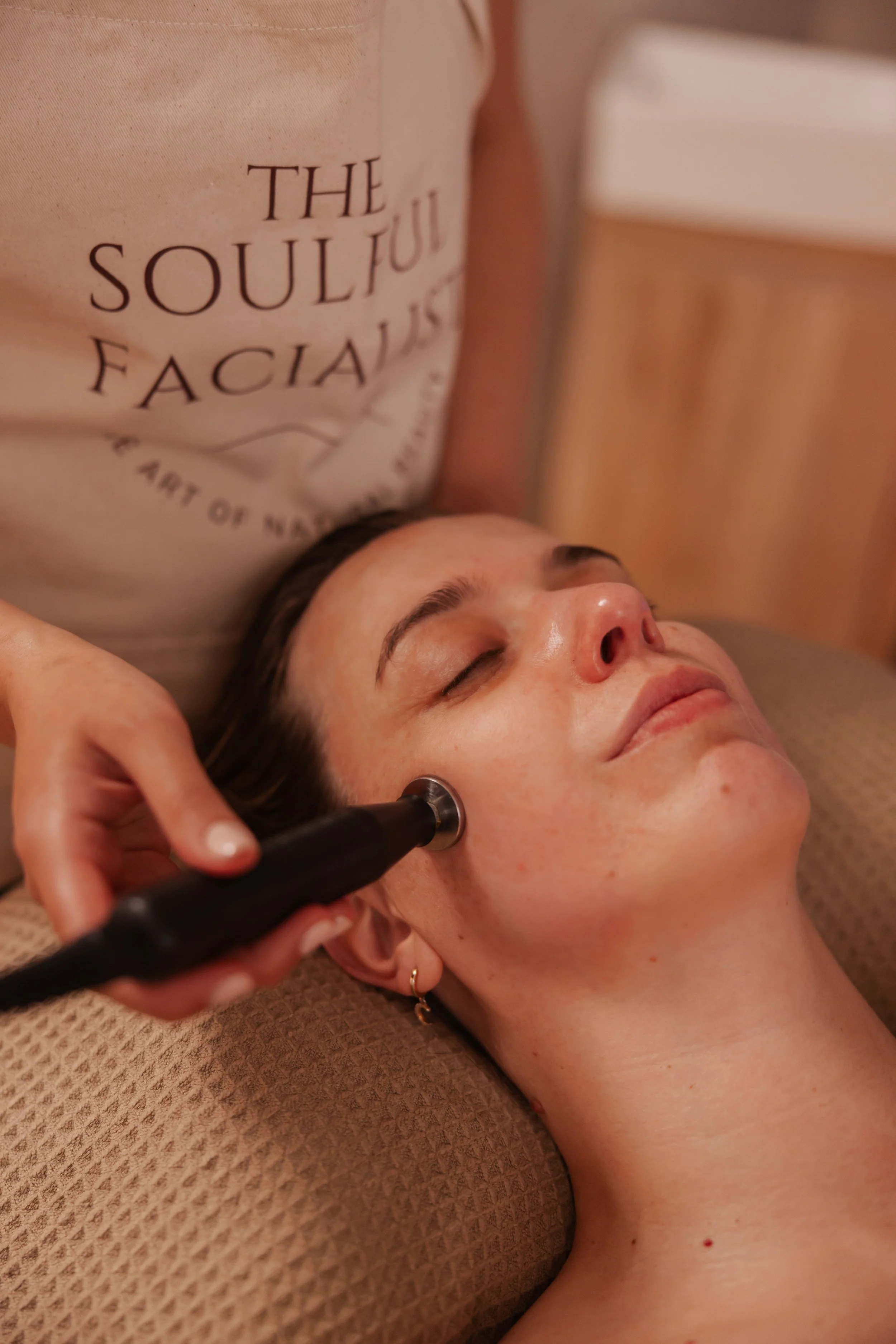 A person receiving a facial treatment in a spa or skincare clinic with skincare products on a tray nearby.