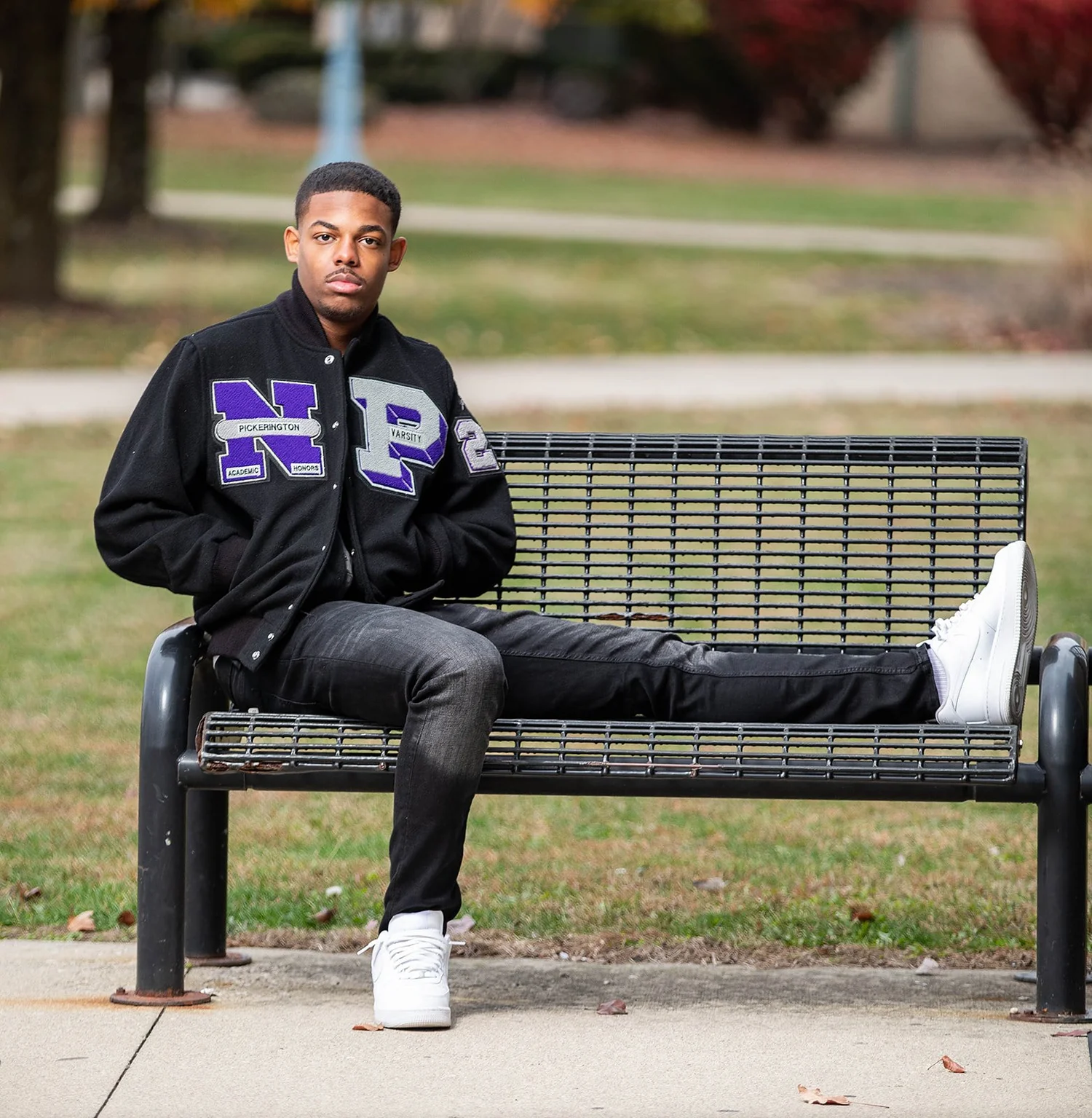 Senior in Pickerington North varsity jacket on a park bench in fall