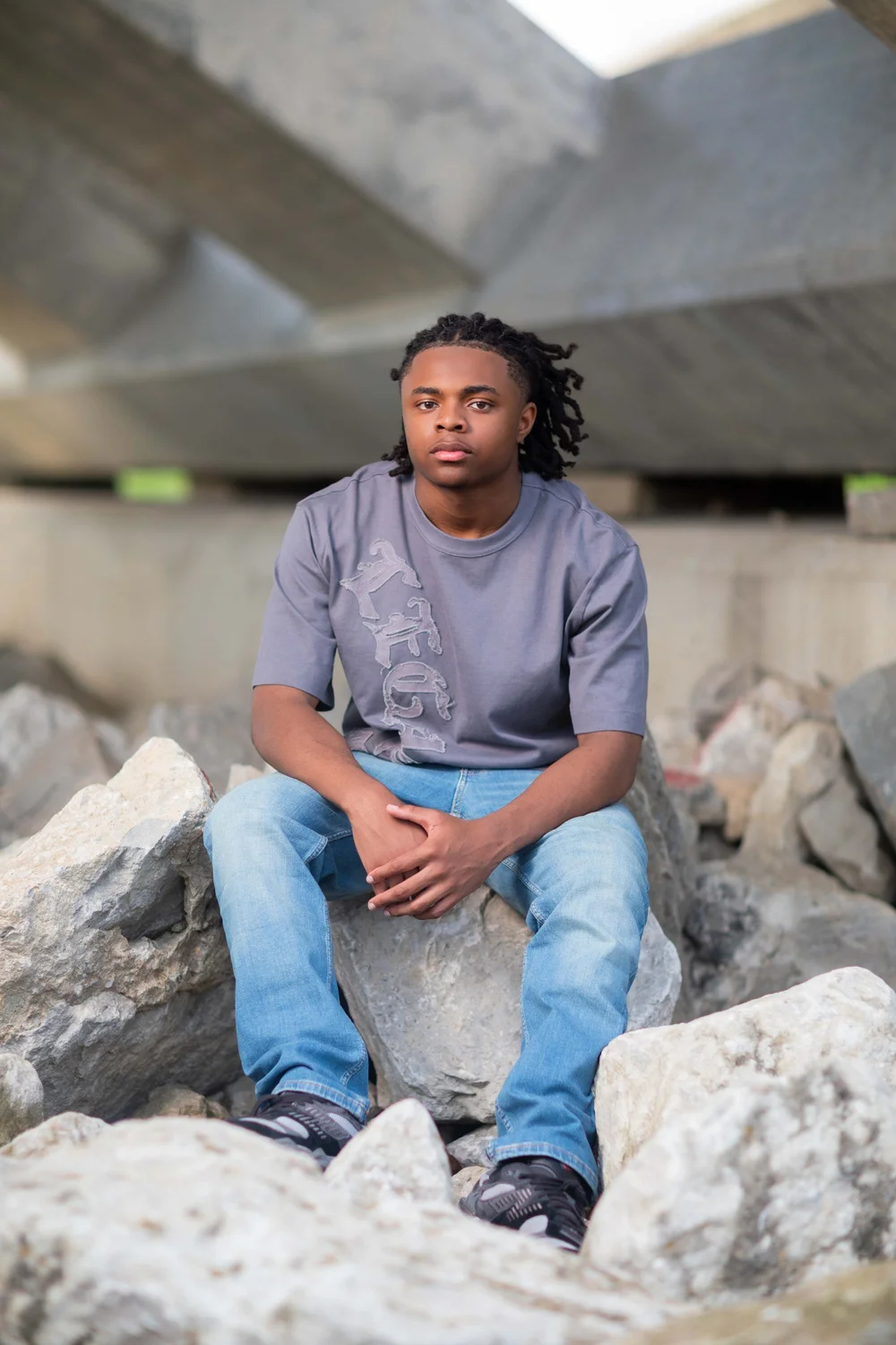 Urban senior portrait on rocks under a bridge