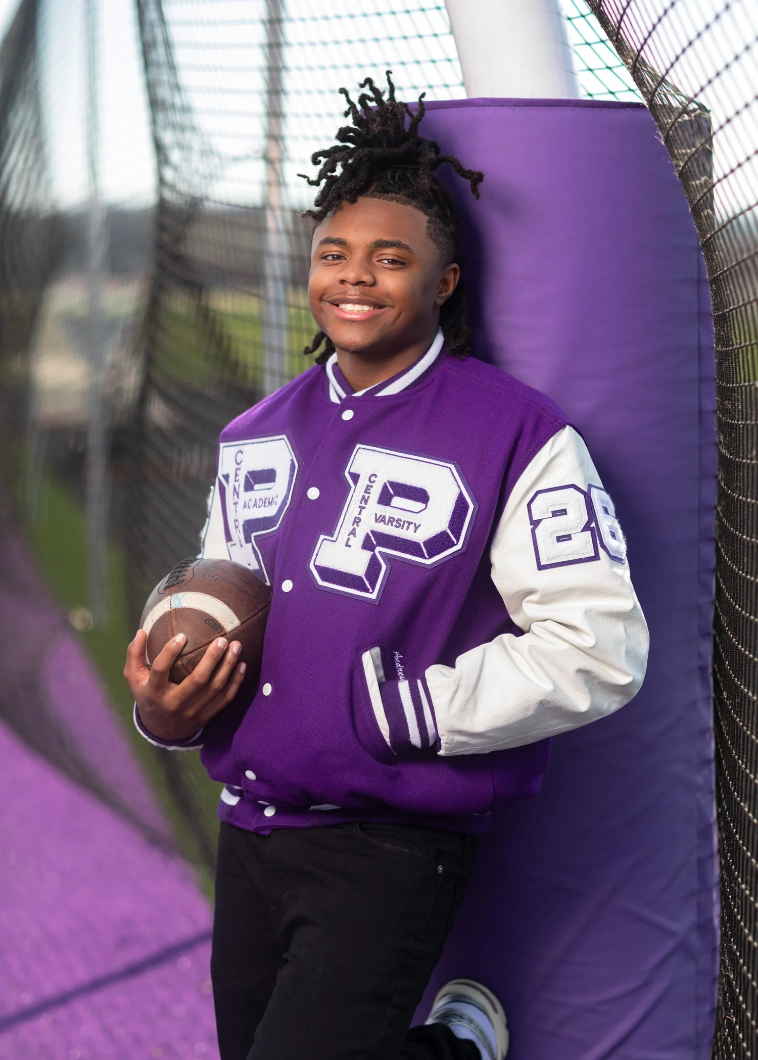 Senior in a purple varsity jacket holding a football, Columbus senior photographer