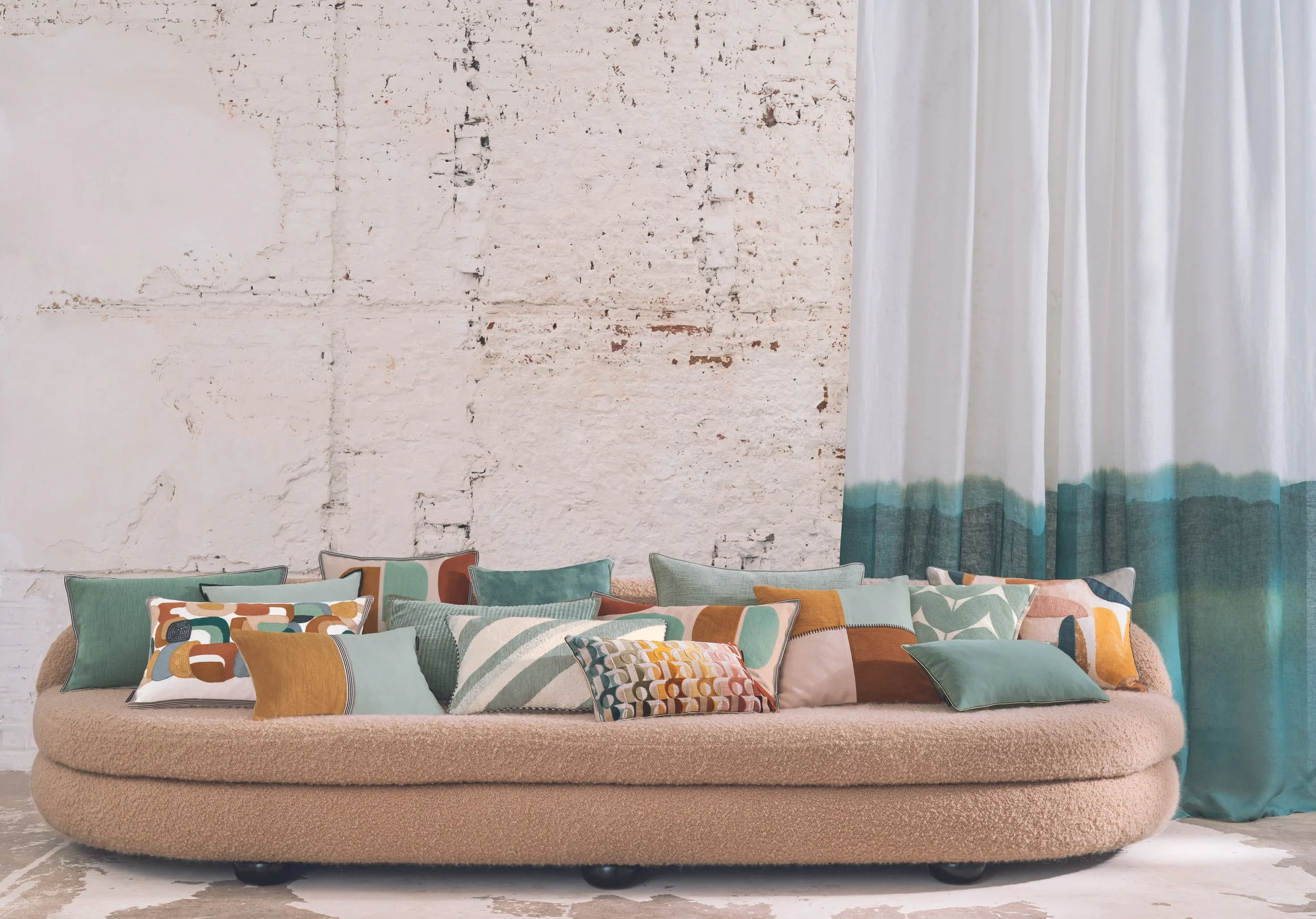 Maison Casamance cushions styled together on a contemporary curved sofa in shades of mineral green, terracotta and ochre.