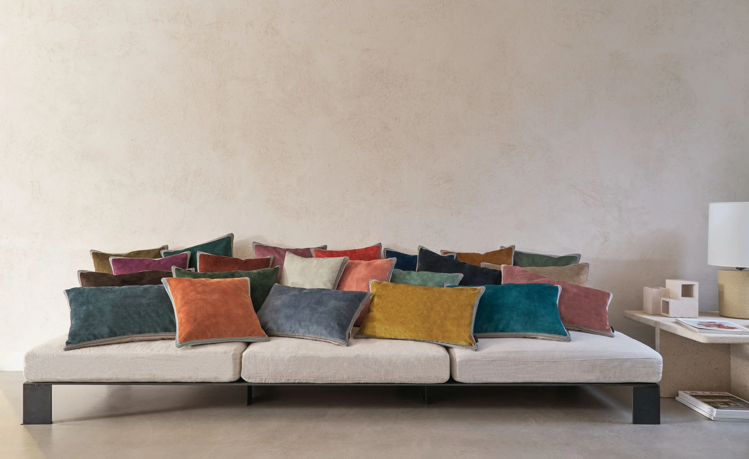 Low sofa lined with Maison Casamance Manade velvet cushions in teal, rust, ochre and pink