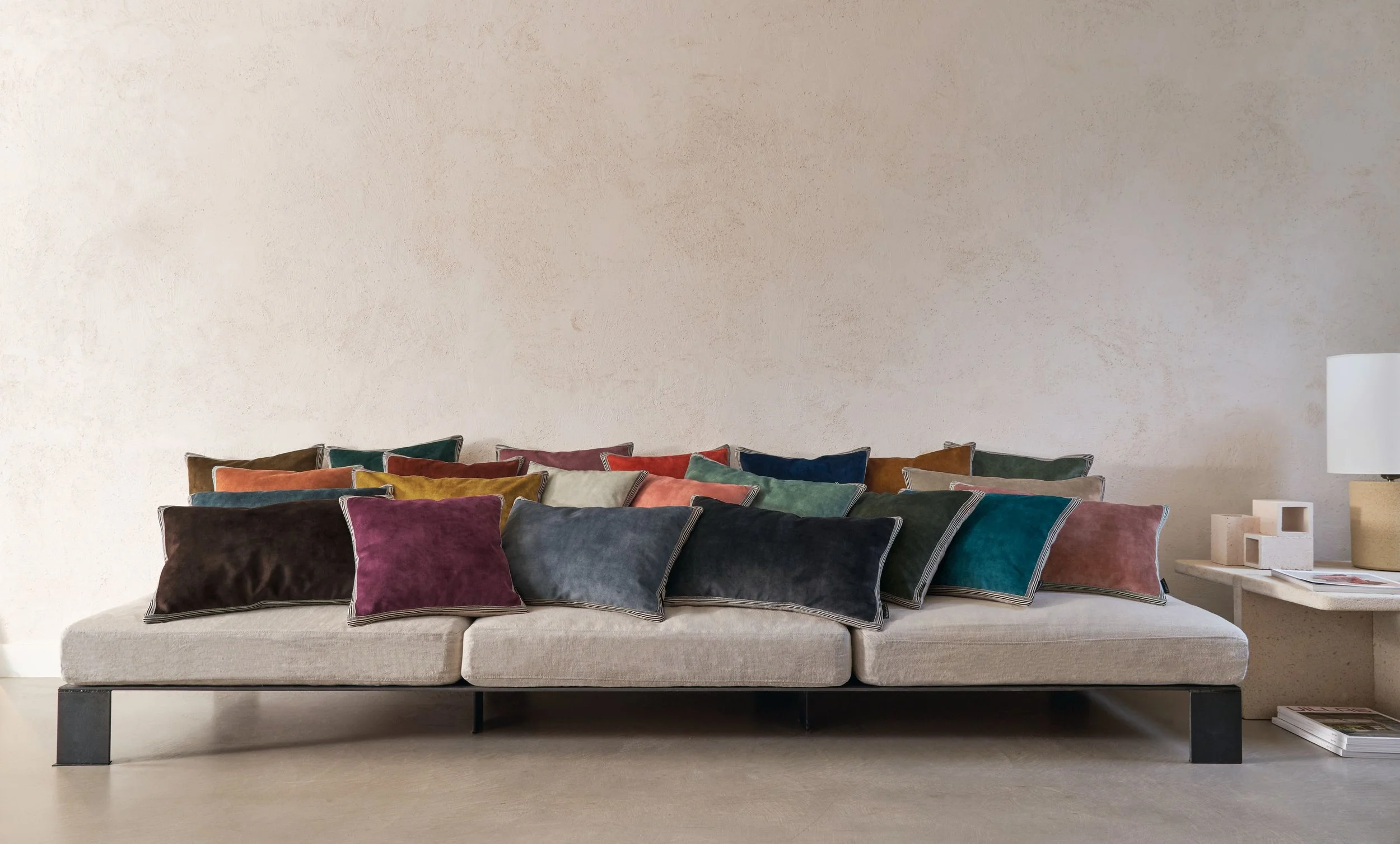 Low white sofa lined with Maison Casamance Manade velvet cushions in plum, grey, teal, rust and navy