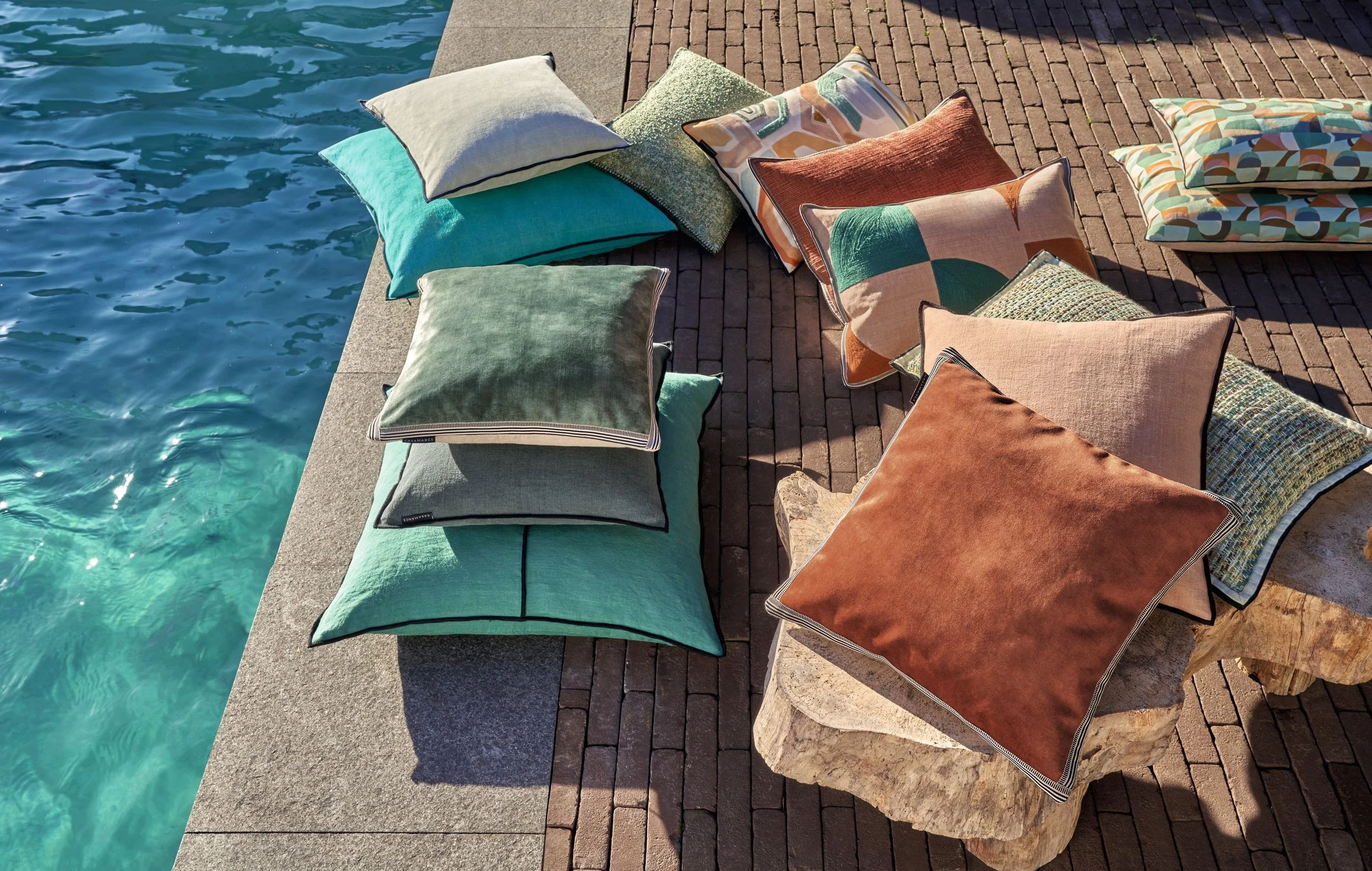 Maison Casamance cushions including Manade velvet in sage, teal and rust piled beside a swimming pool