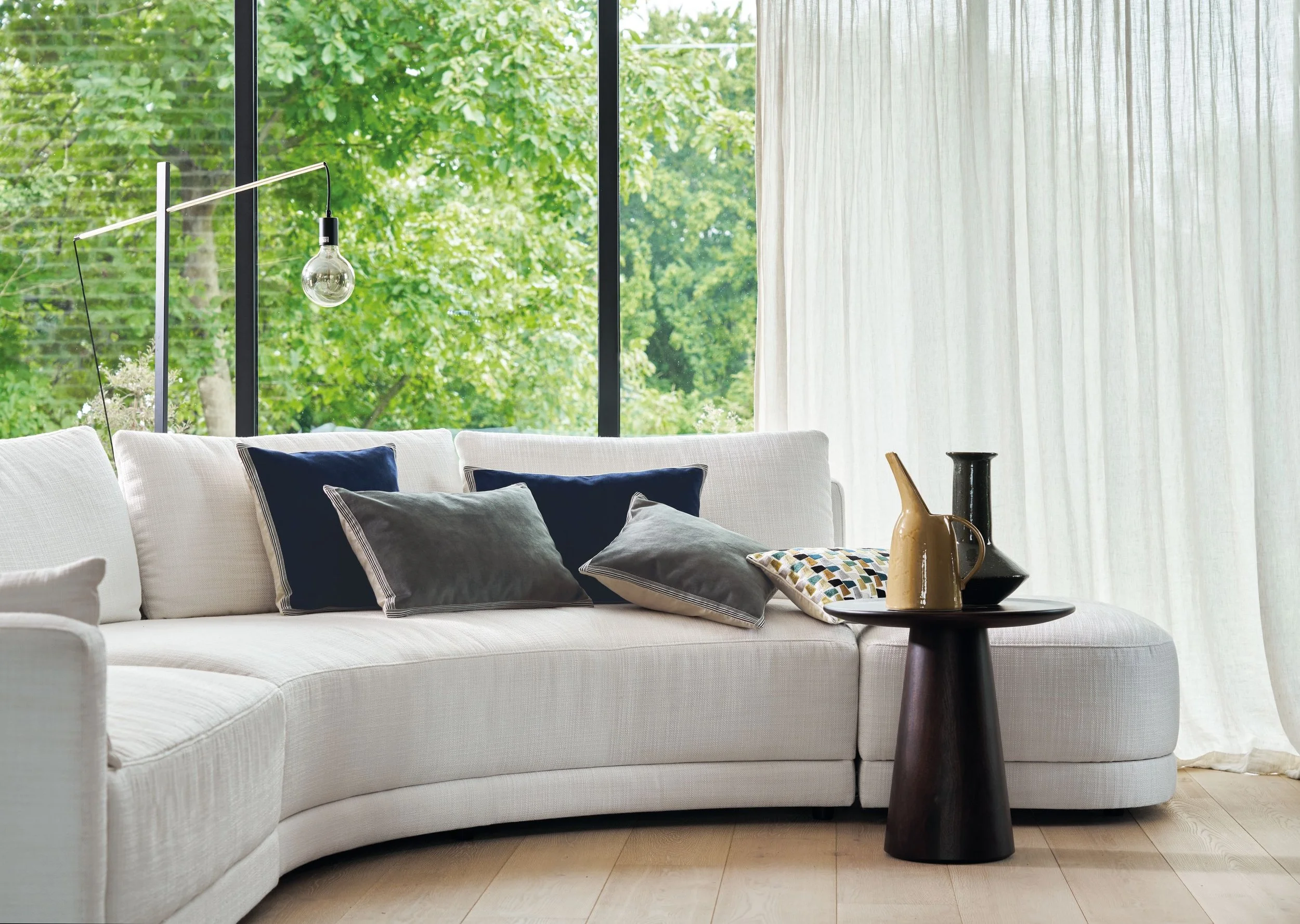Curved white sofa with Maison Casamance Manade cushions in navy and charcoal grey