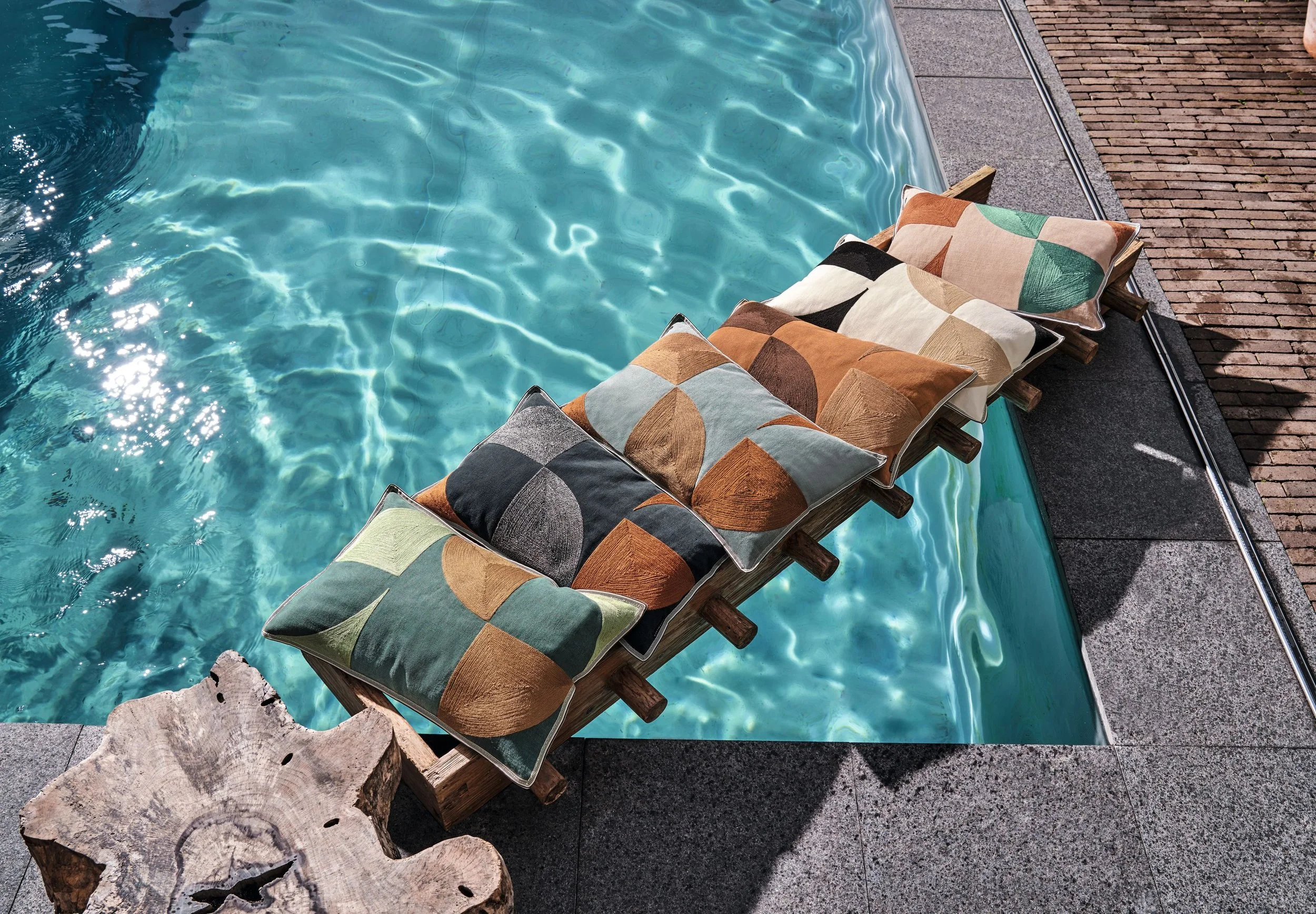 Maison Casamance Coconut embroidered cushions piled beside a swimming pool