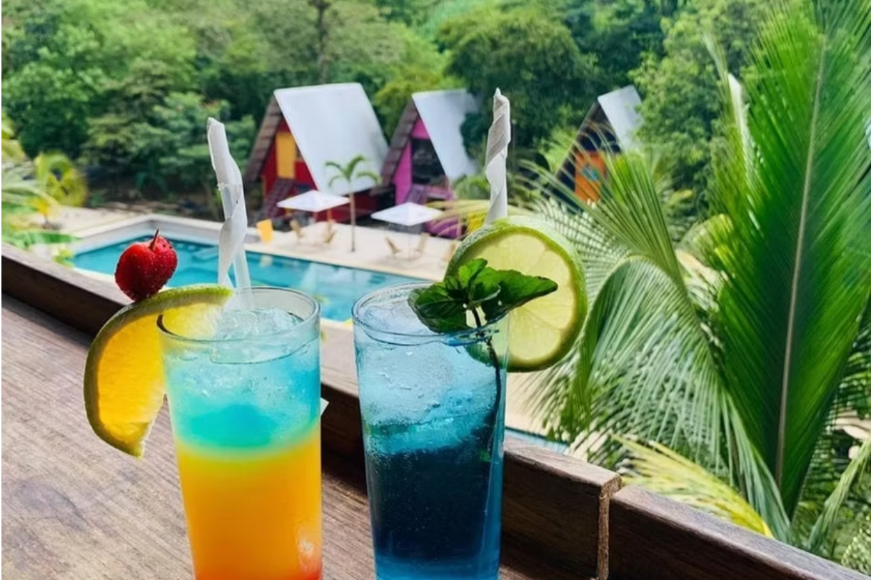 Two tropical cocktails are on a table overlooking the pool and cabins at a hotel in Semuc Champey