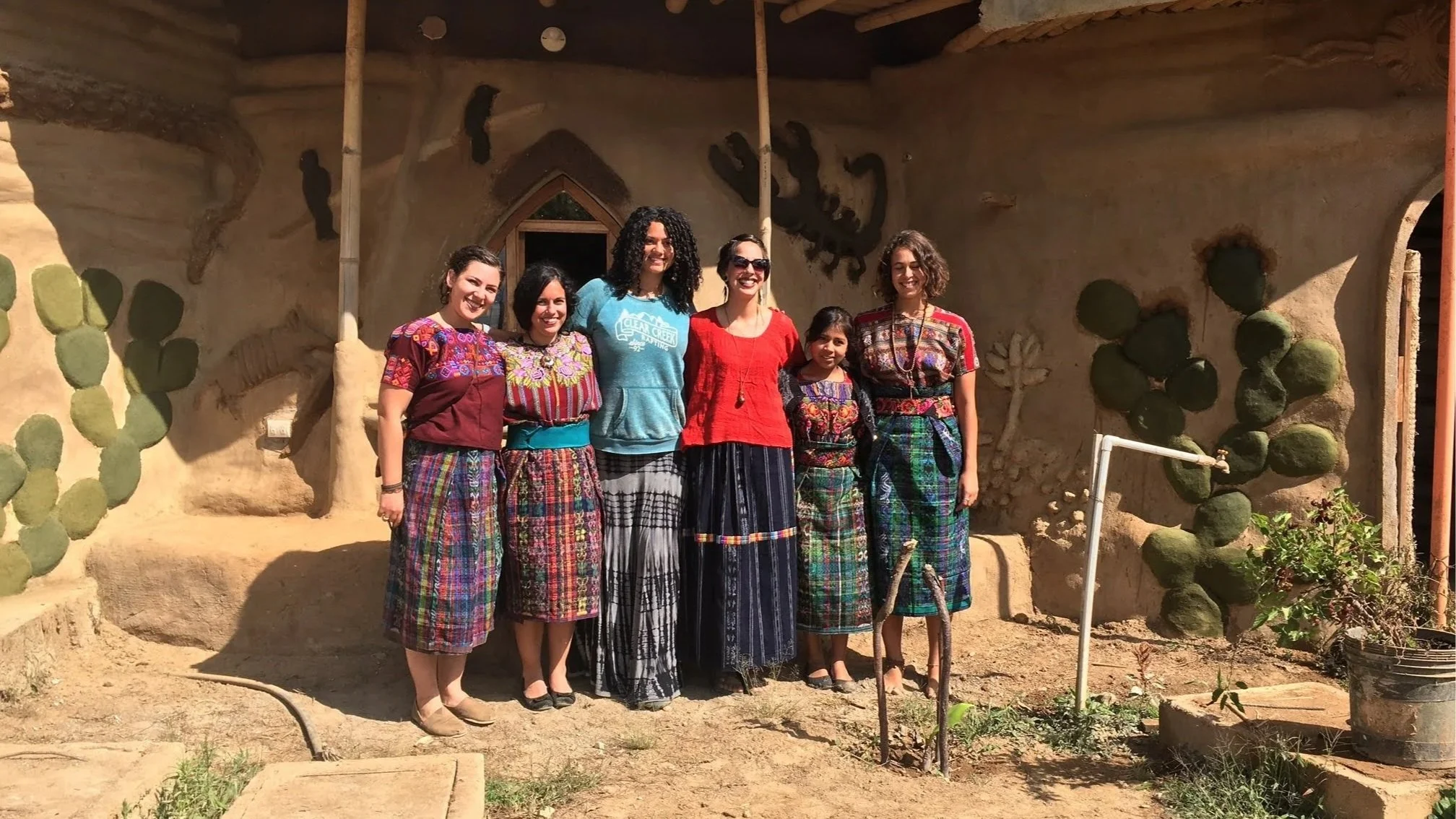 A group of women are doing ecotourism in Guatemala while in front of a clay house dressed in traditional clothing