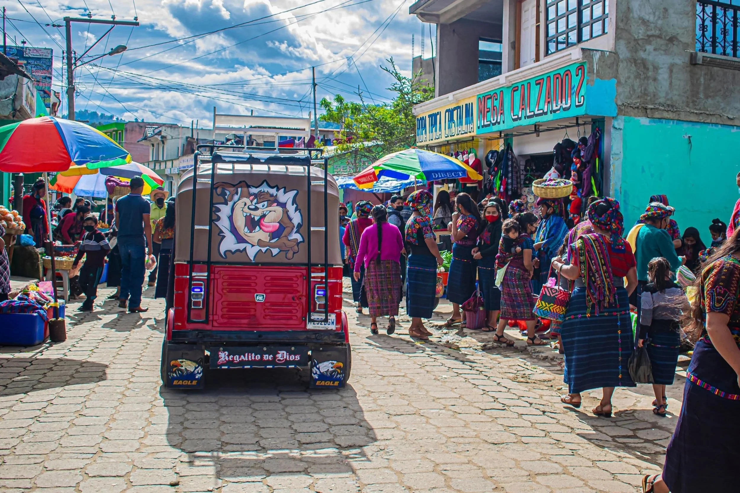 A busy market street in Xela, Guatemala, with a tuktuk and women dressed in traditional clothing