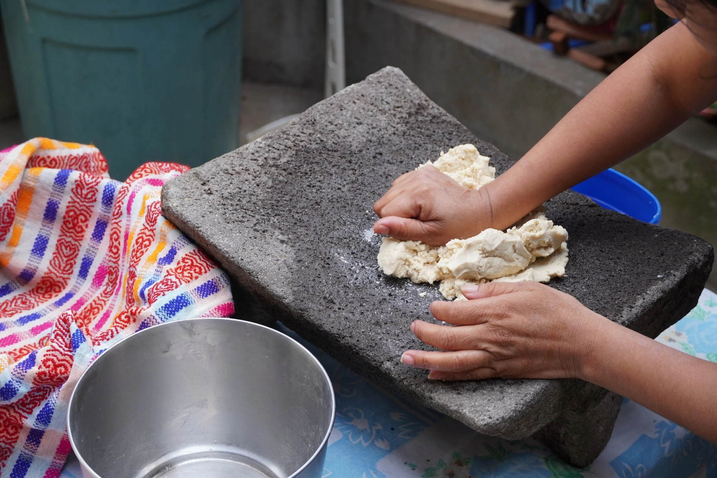 Hands are pounding masa on a stone in Guatemala while making tortillas, a vegan food in Guatemala