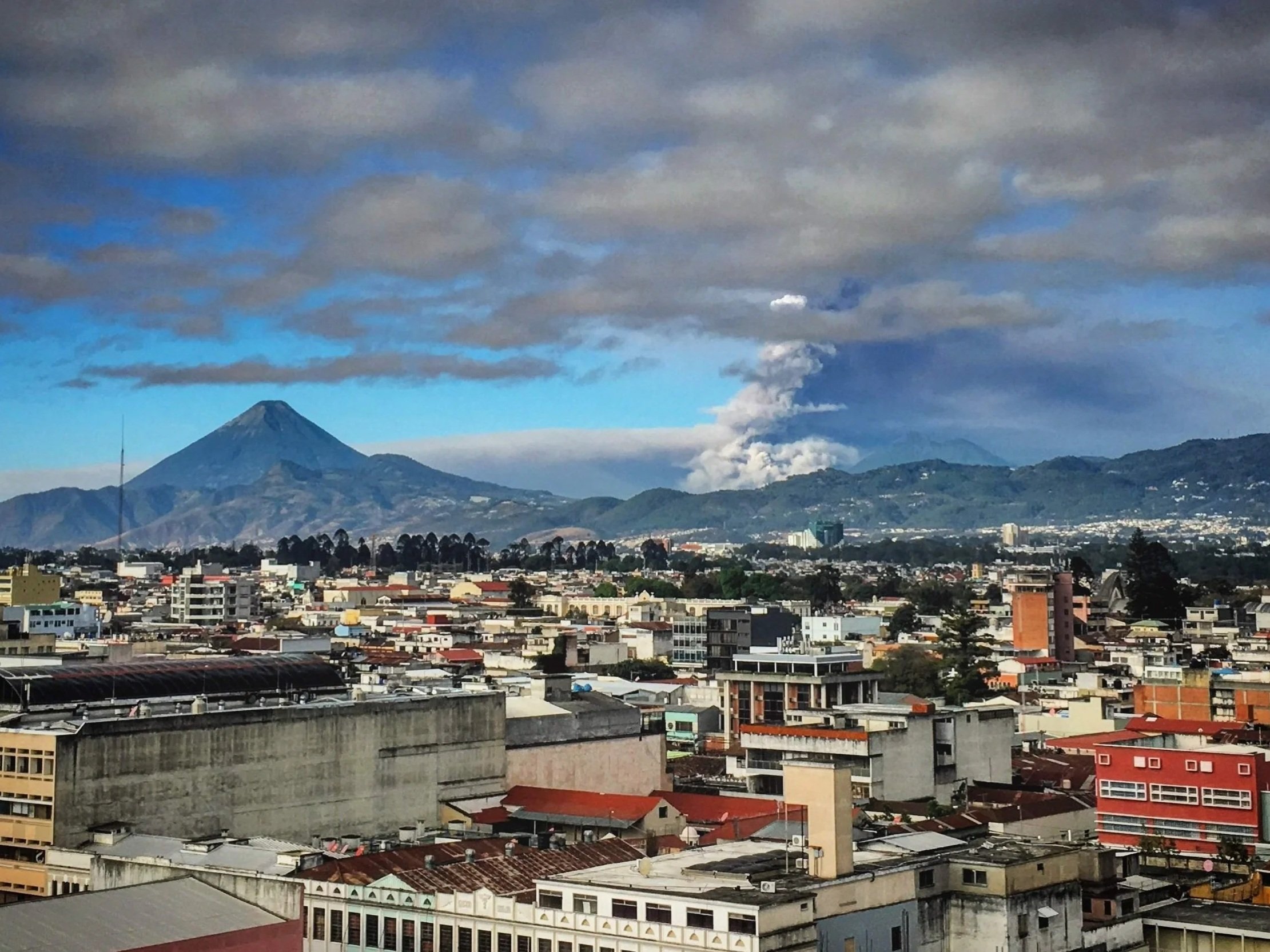 Warm Guatemala weather with a volcano is puffing smoke into the air beyond the cityscape