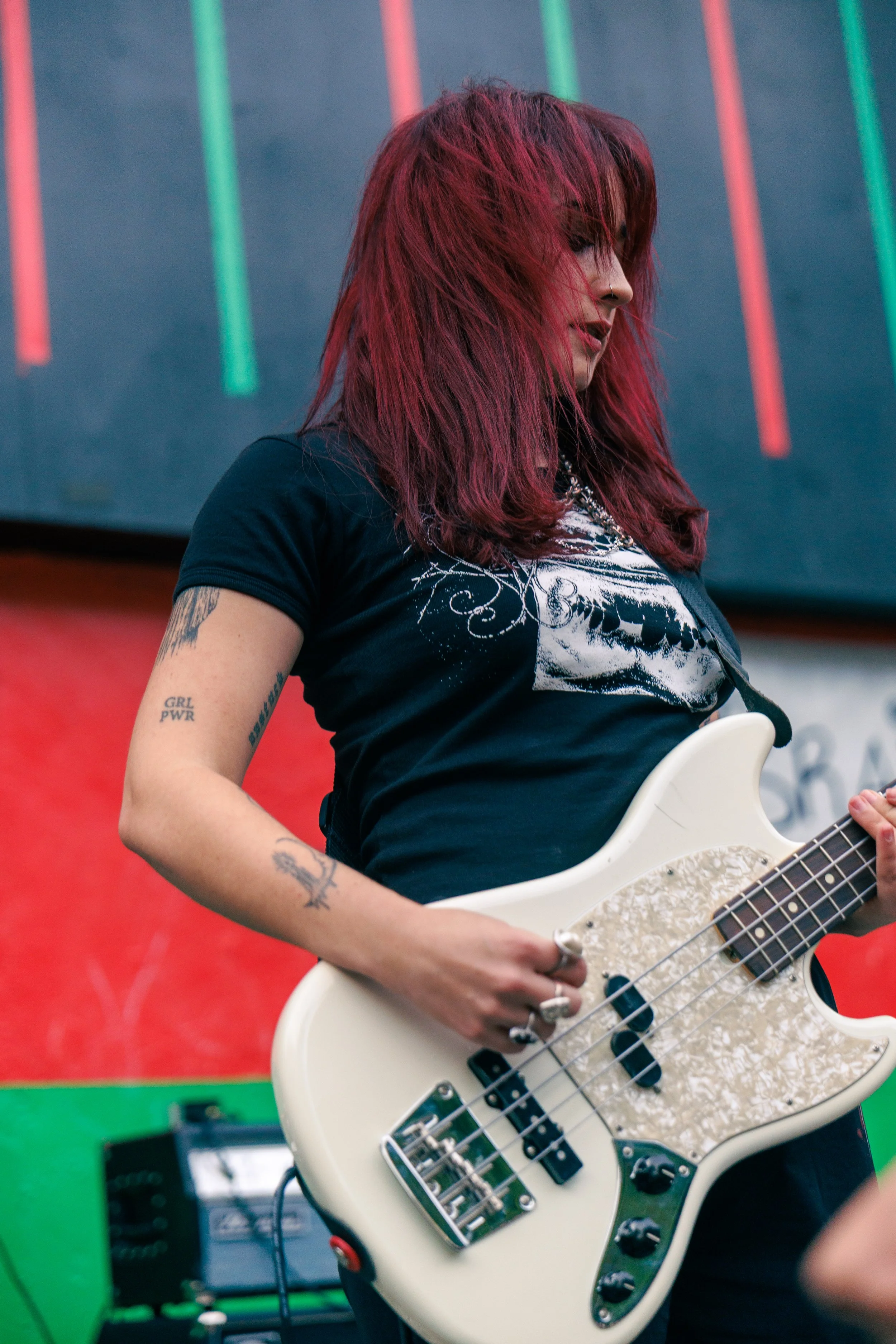 A person with red hair playing a white electric guitar in front of a colorful background.