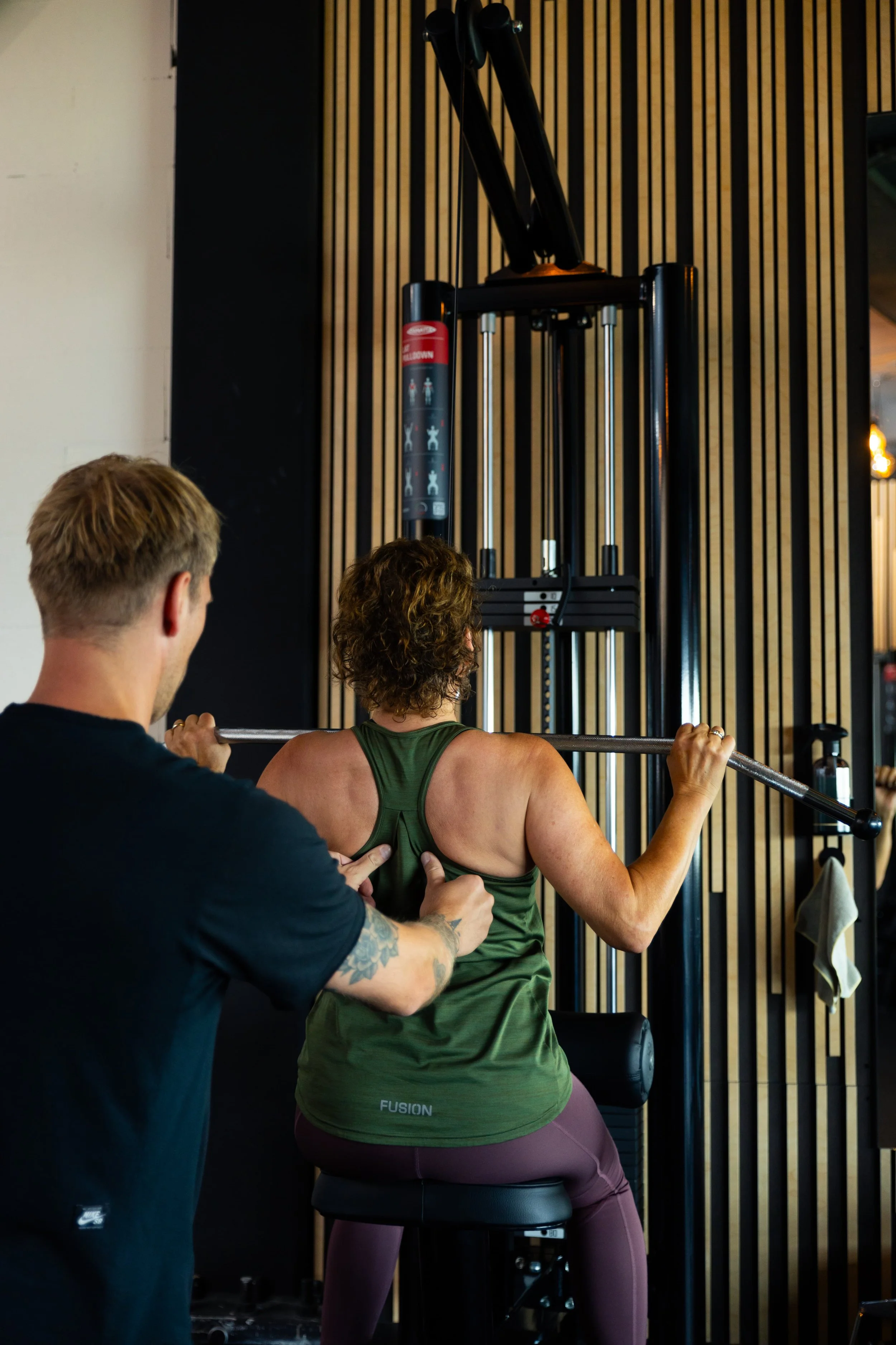 Een man die een vrouw helpt bij het uitvoeren van een squatoefening in een sportschool.