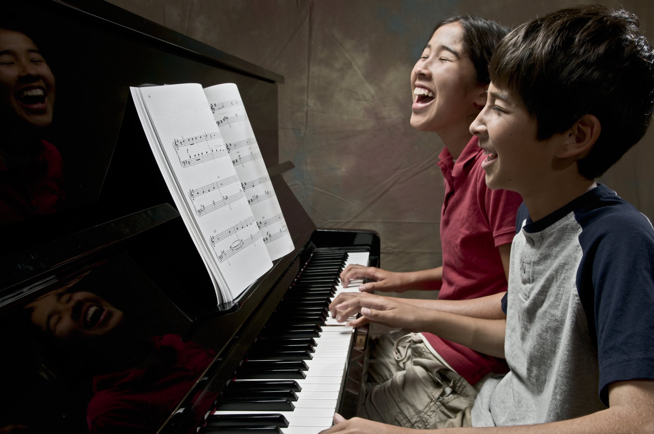 Two people laughing while playing piano together