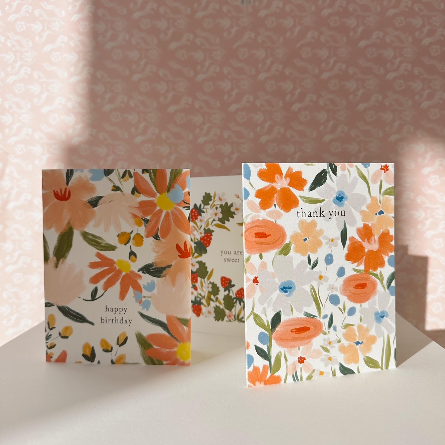 Three floral greeting cards on a white surface, featuring designs with various colorful flowers. The cards are labeled "happy birthday," "thank you," and "you are sweet."
