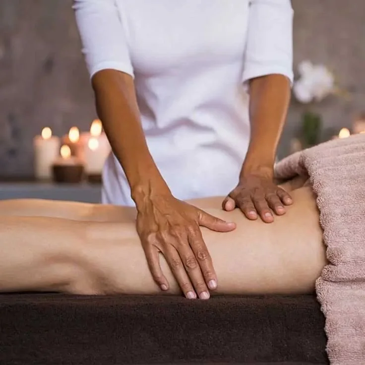 A healthcare professional in blue scrubs and white gloves examining or tending to a patient's leg and foot in a medical setting.