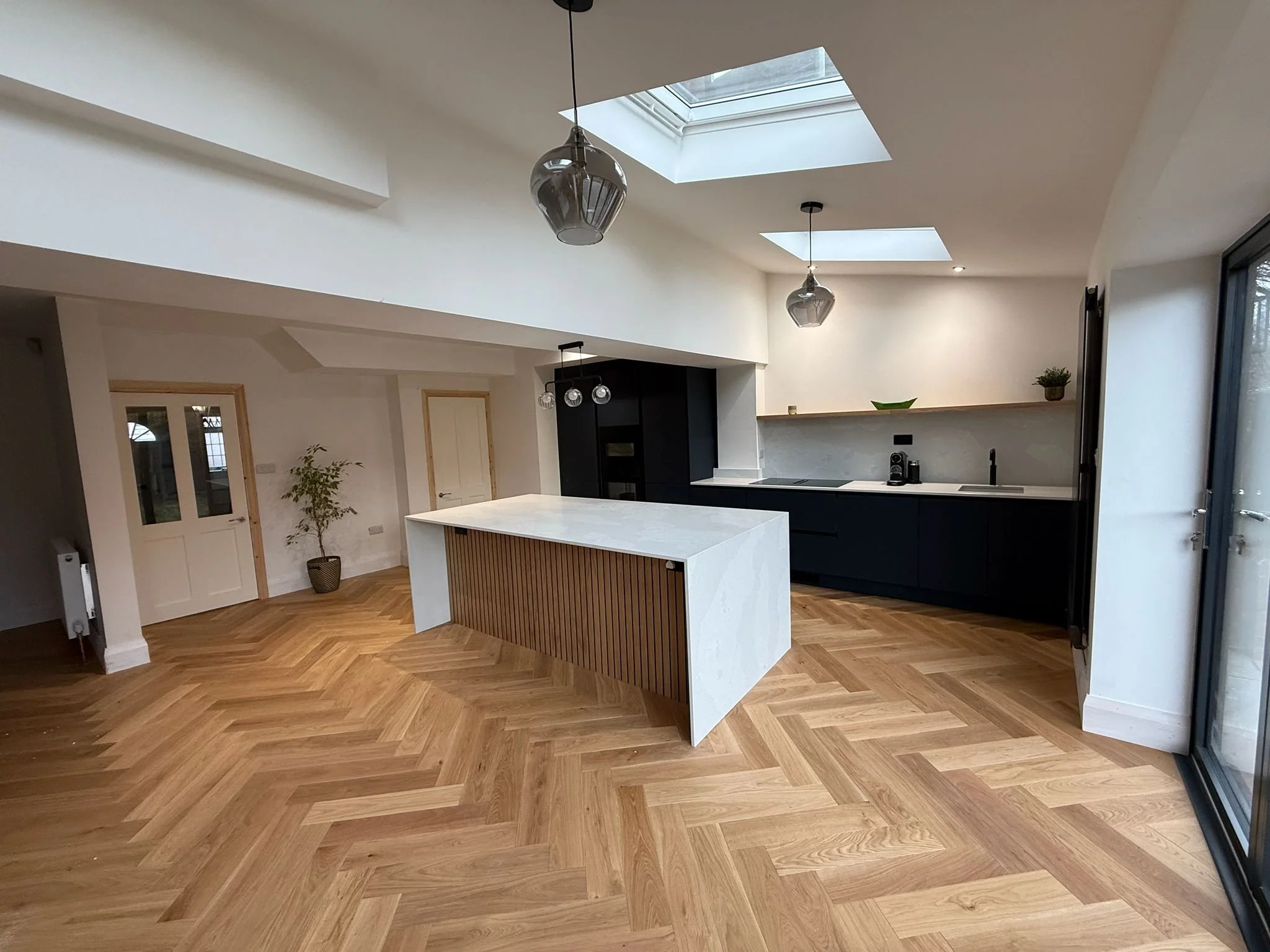 Modern kitchen with a white island, black cabinets, skylights, pendant lights, and hardwood floors.