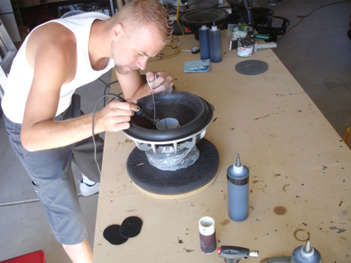 A man working on a speaker in a workshop, using tools to modify the speaker cone.
