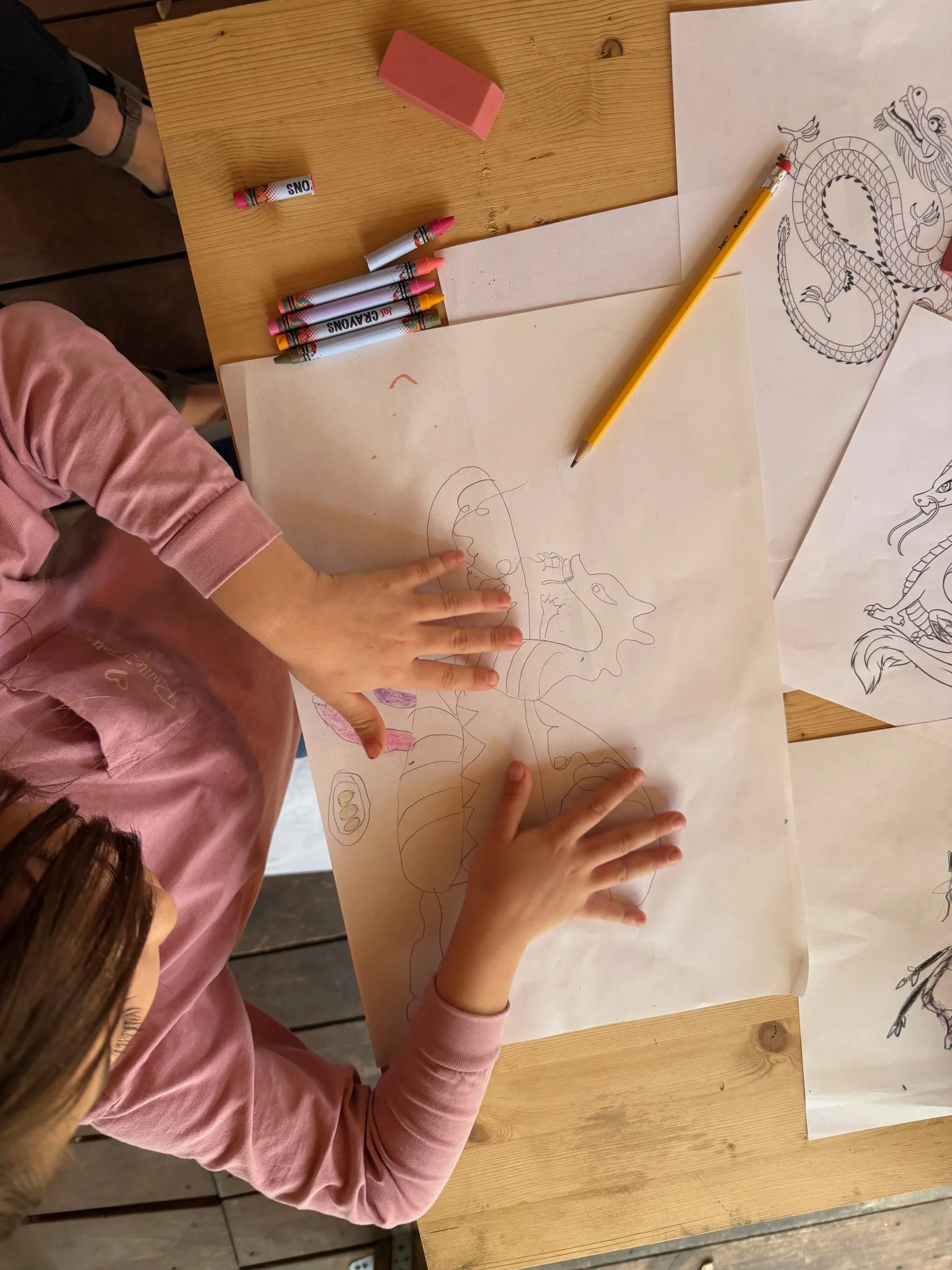 Children drawing on large sheets of paper, working on a colorful art project with markers and crayons on a wooden table.