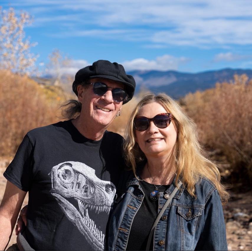 Gary Storm and Linda Storm are outdoors in Santa Fe with mountains in the background. Photo by Michel Lee Jackson