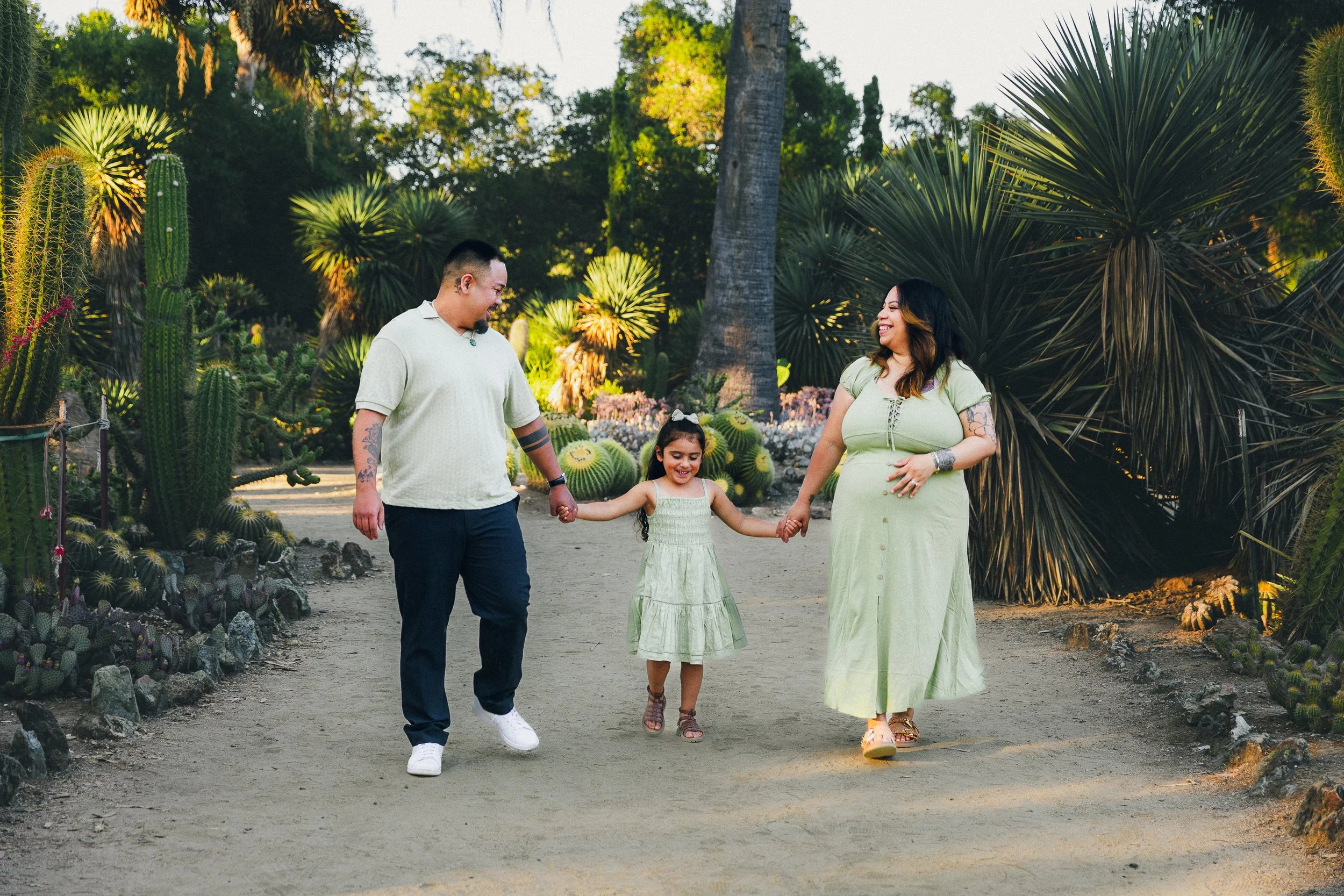 A family of three walking hand in hand in a desert garden with cacti and large succulents, smiling and enjoying their time together.