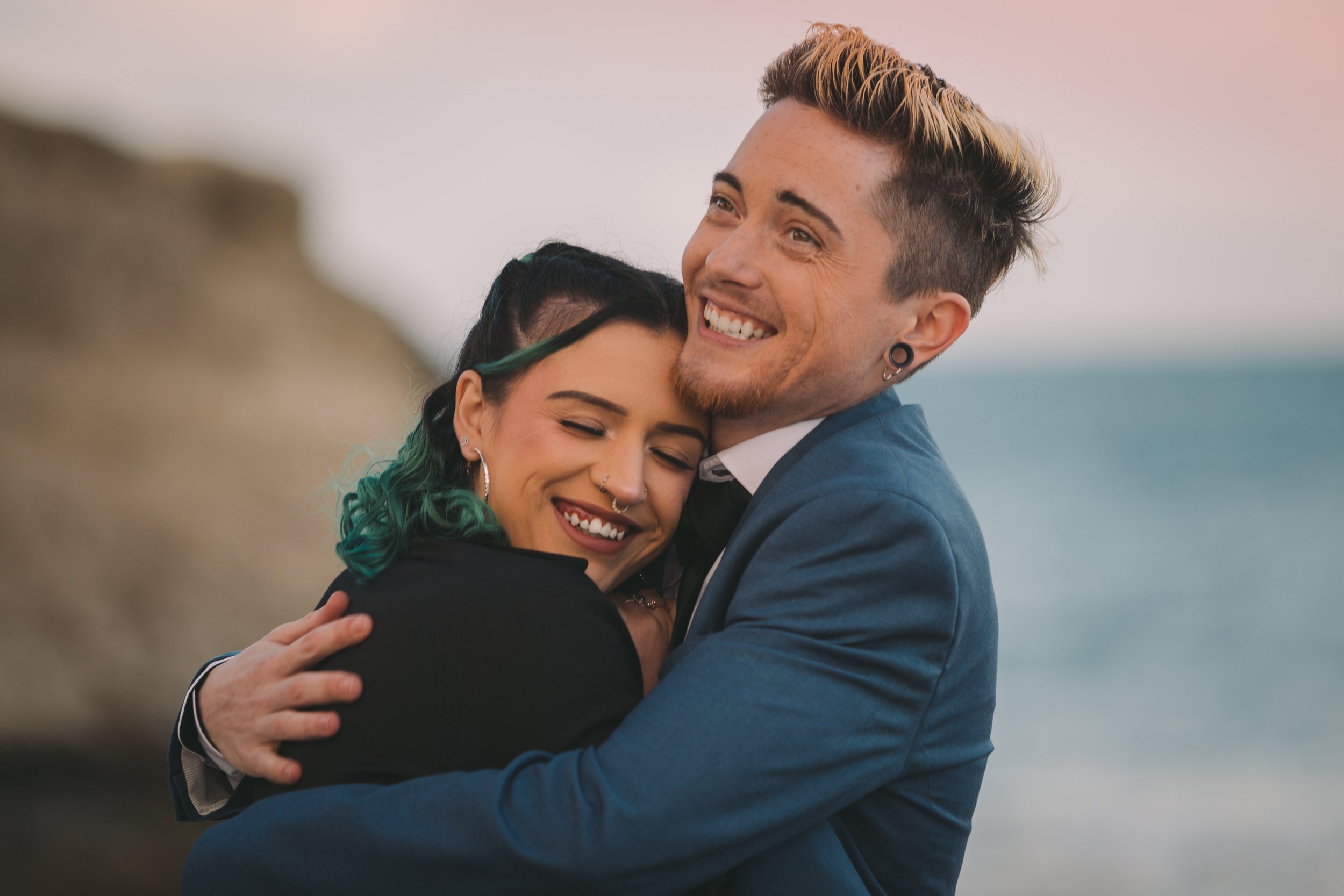 A young couple hugging and smiling by the beach at sunset.