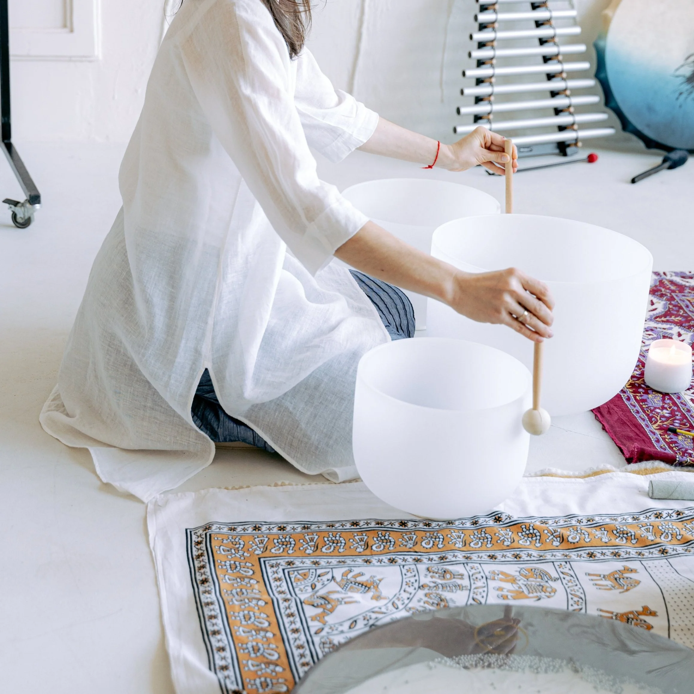 person kneeling on the ground next to three crystal singing bowls. they're playing them with rubber malets