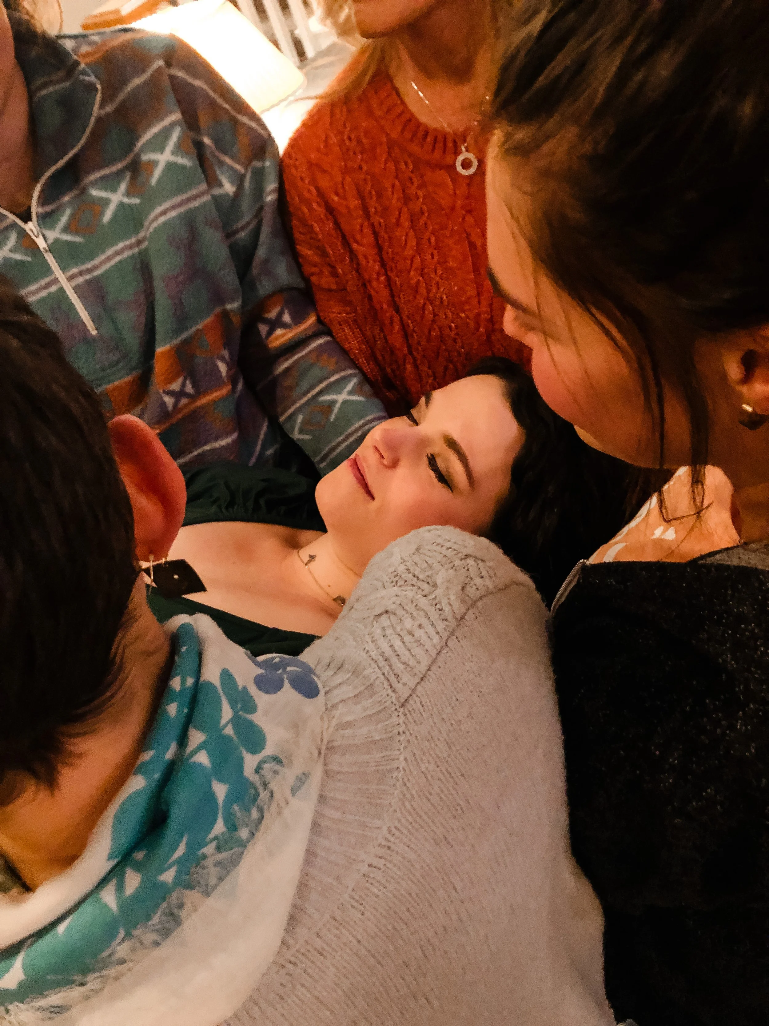 a close up on a huddle of women holding a pregnant woman and singing to her