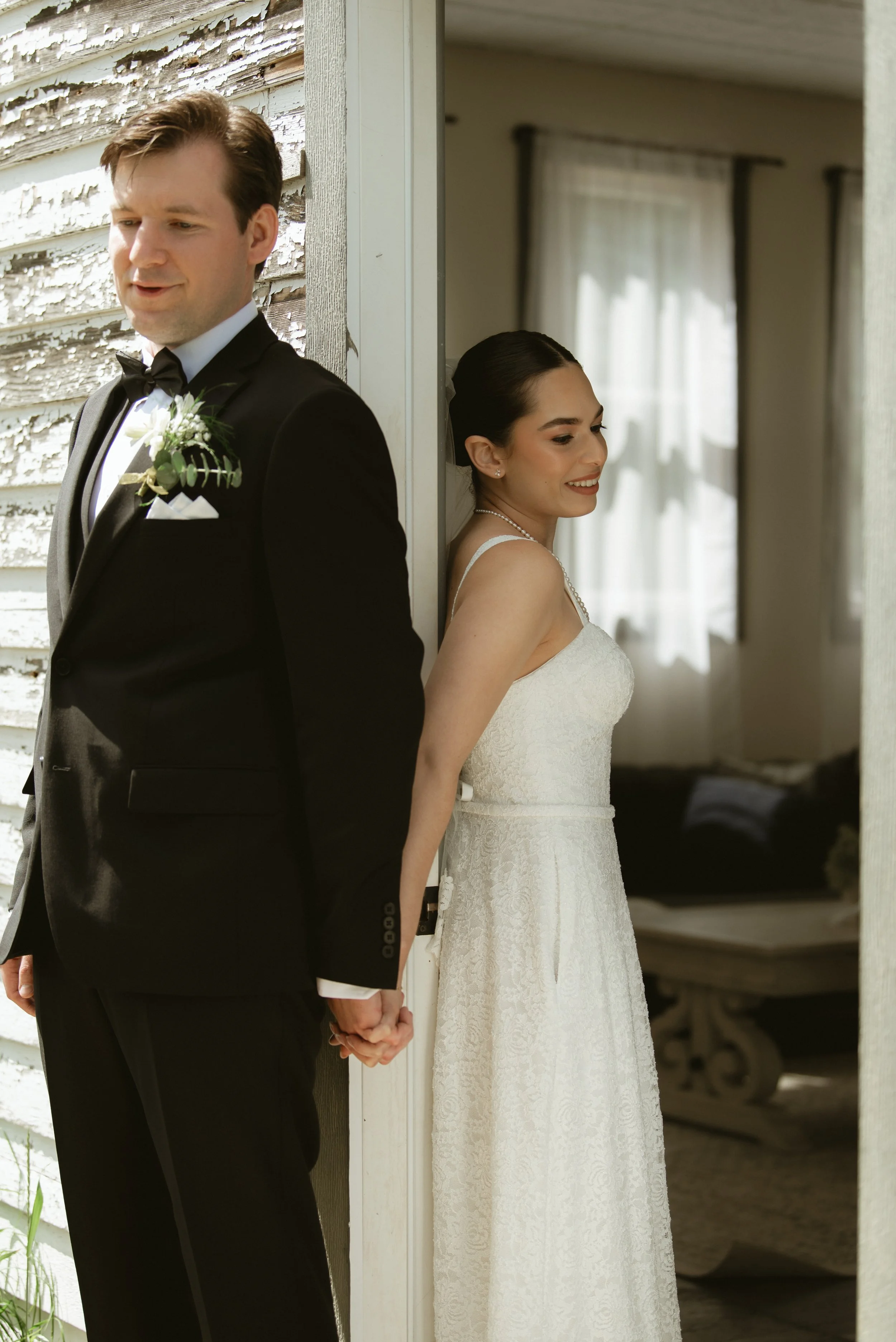 Bride and groom holding hands around a doorway before their first look at Pine & Pond Wedding Venue in Ponoka County, Alberta photographed by Danielle Aichelle Photographed