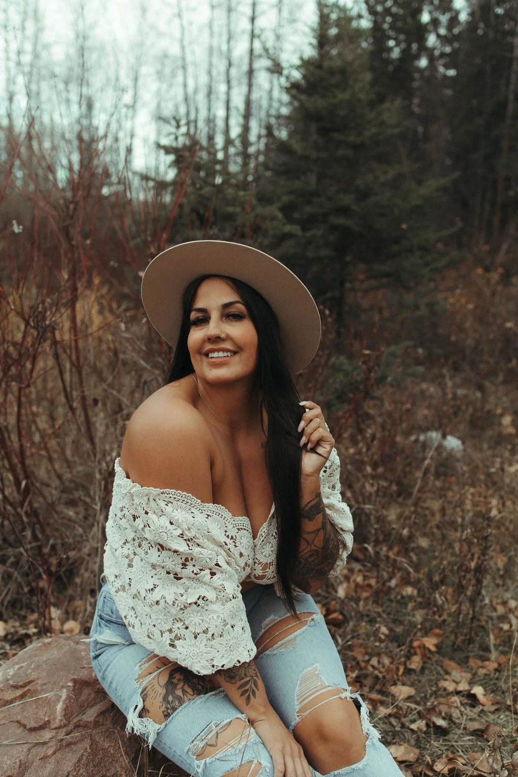 Portrait of a woman wearing a wide-brimmed hat while sitting outdoors in a wooded area.