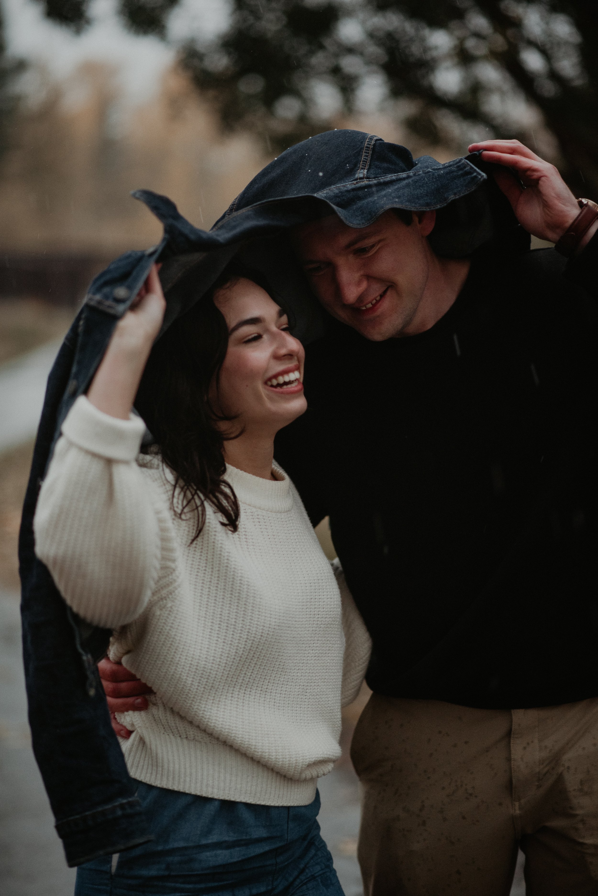 Couple laughing together while sharing a jacket during a rainy engagement session in Red Deer, Alberta, photographed by Danielle Aichelle Photography