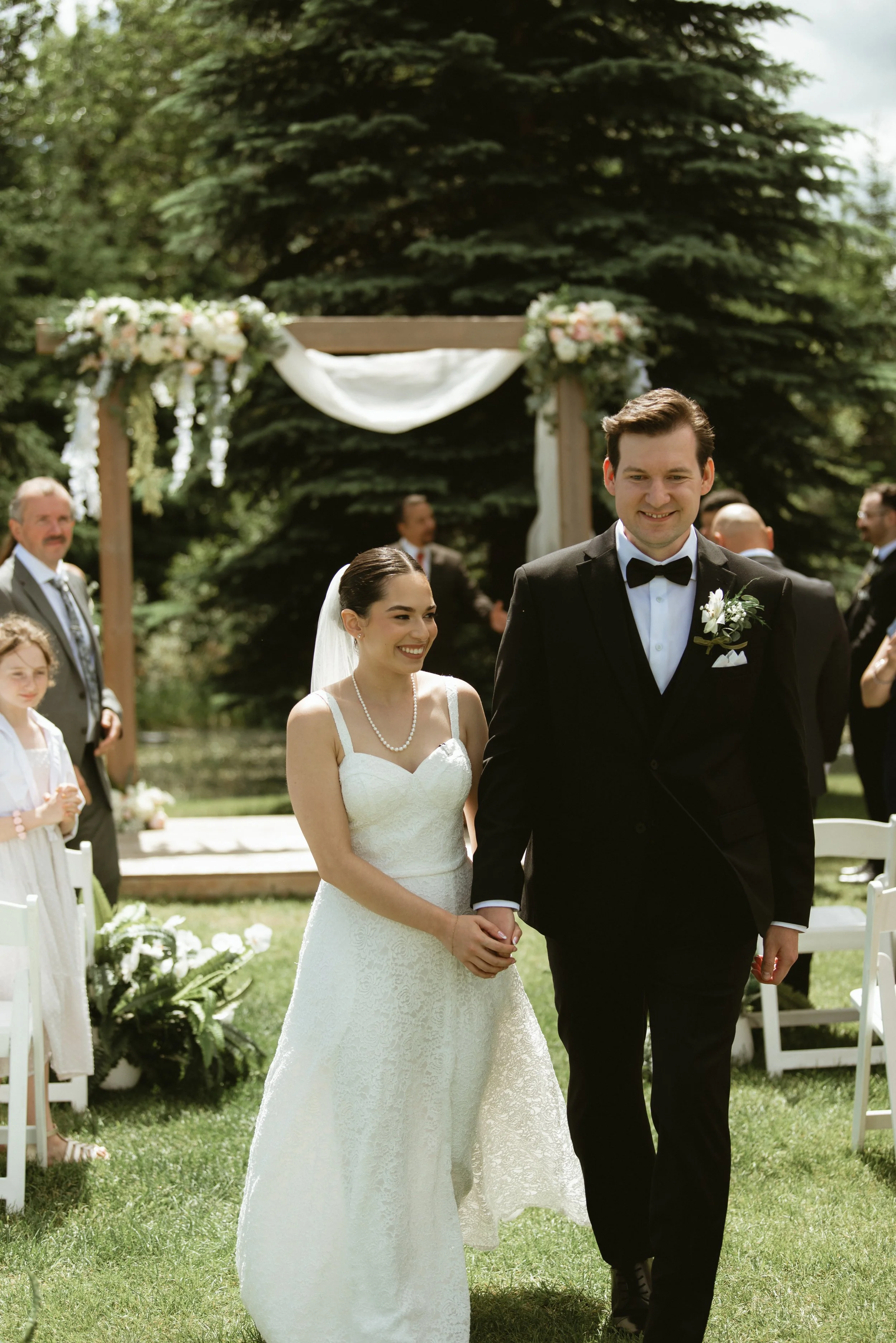 Bride and groom walking hand in hand down the aisle after their outdoor wedding ceremony at Pine & Pond  Wedding Venue in Ponoka County, Alberta, photographed by Danielle Aichelle Photography