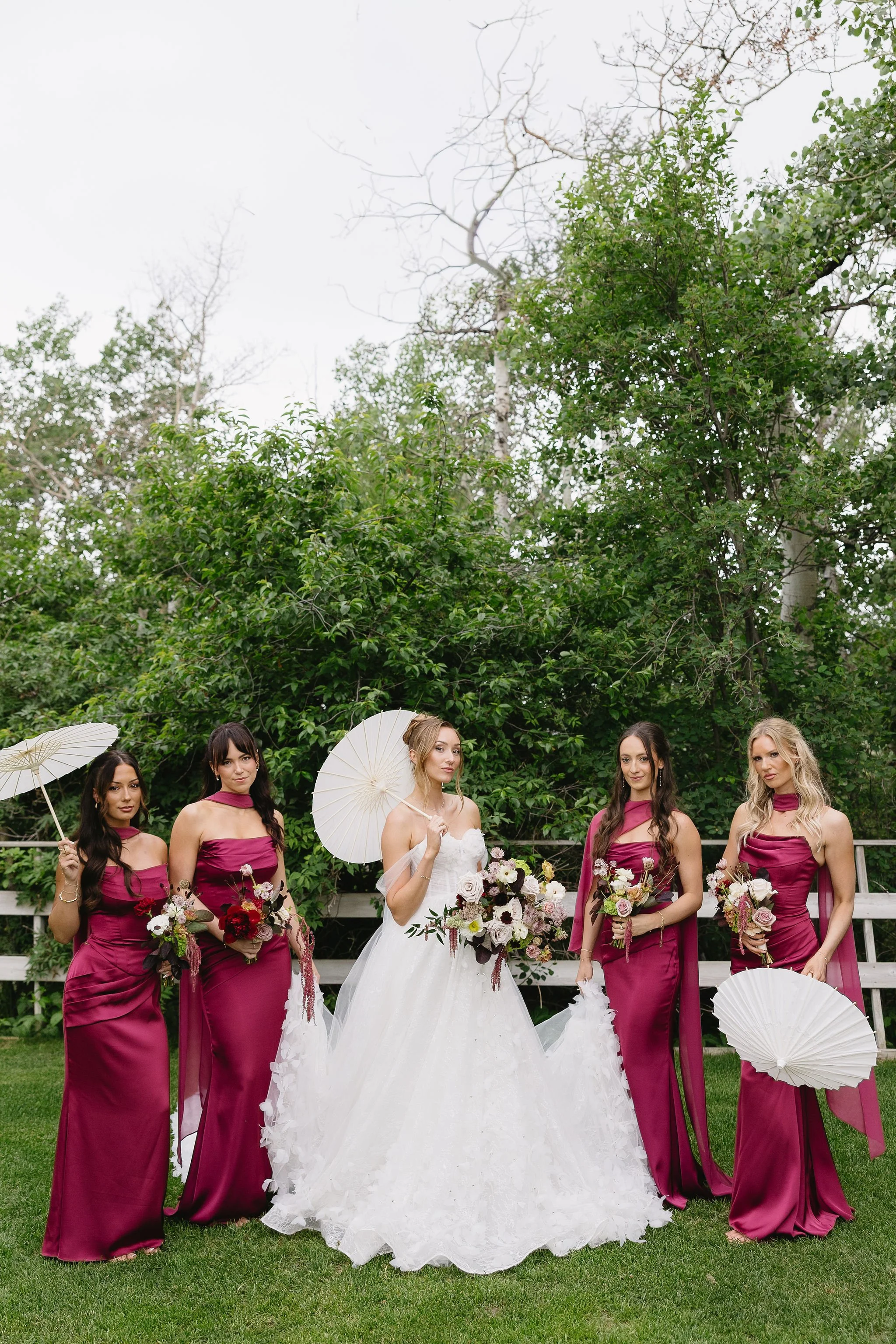 Bride and bridesmaids posing outdoors with bouquets at Hilltop Wedding Center in Sylvan Lake, Alberta, with bridal hair styled by Danielle Aichelle Artistry