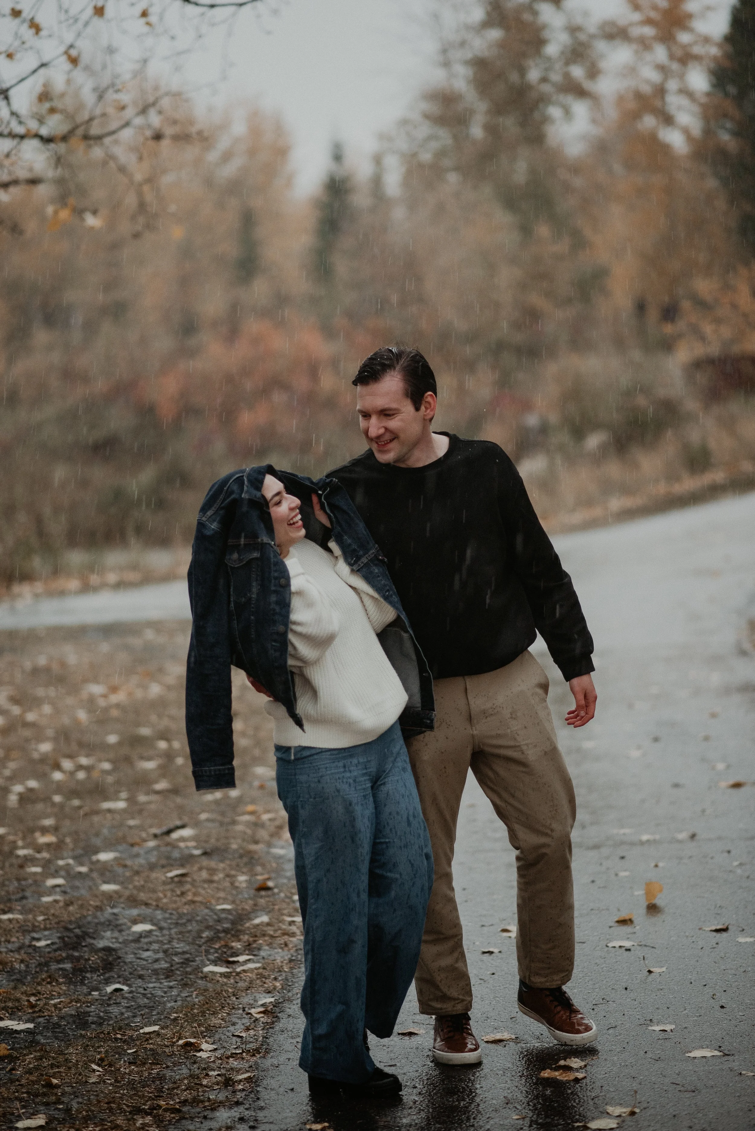 Couple laughing together during a rainy engagement session at McKenzie Trails in Red Deer, Alberta, photographed by Danielle Aichelle Photography