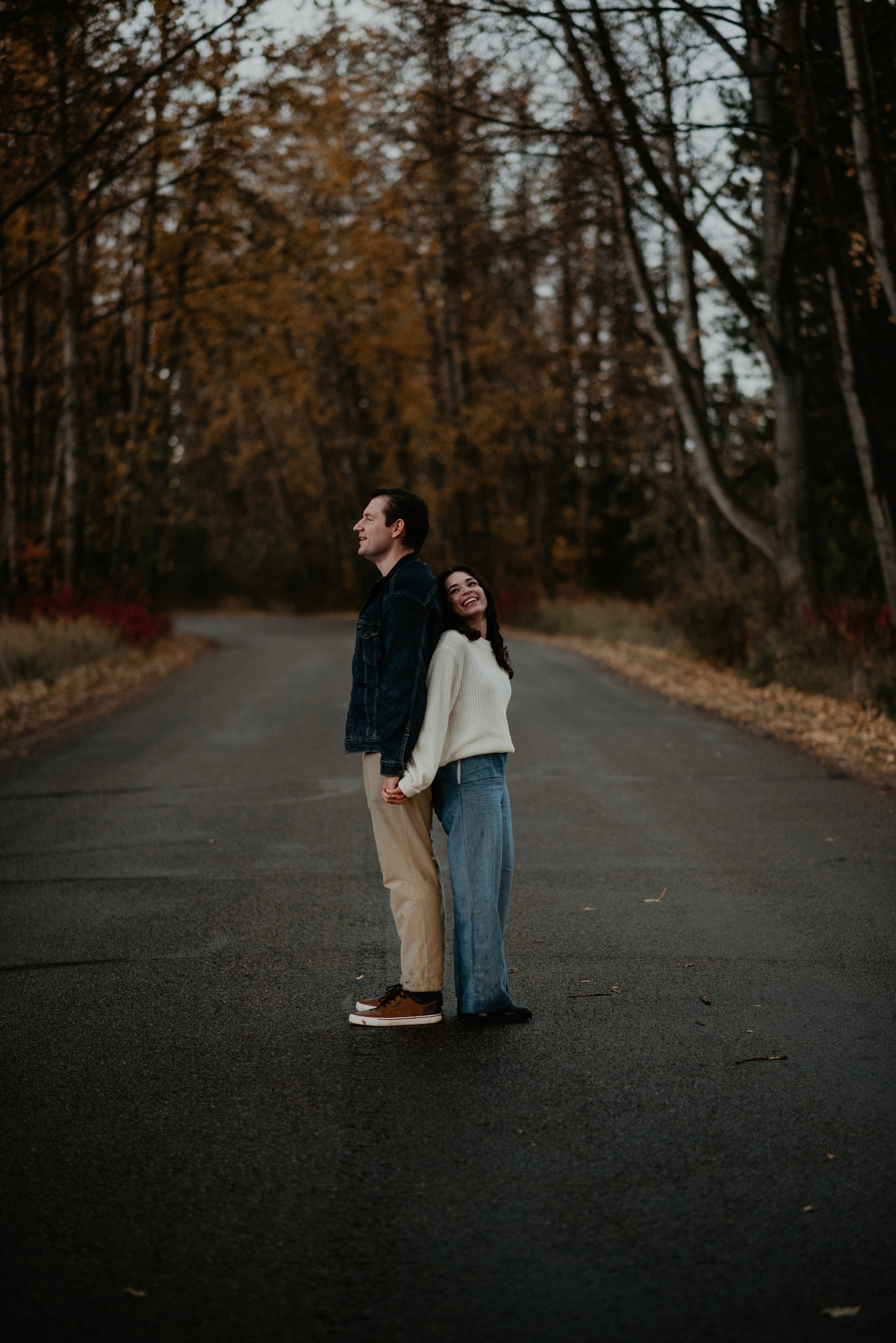 Couple holding hands on a quiet road during their engagement session at McKenzie Trails in Red Deer, Alberta, photographed by Danielle Aichelle Photography