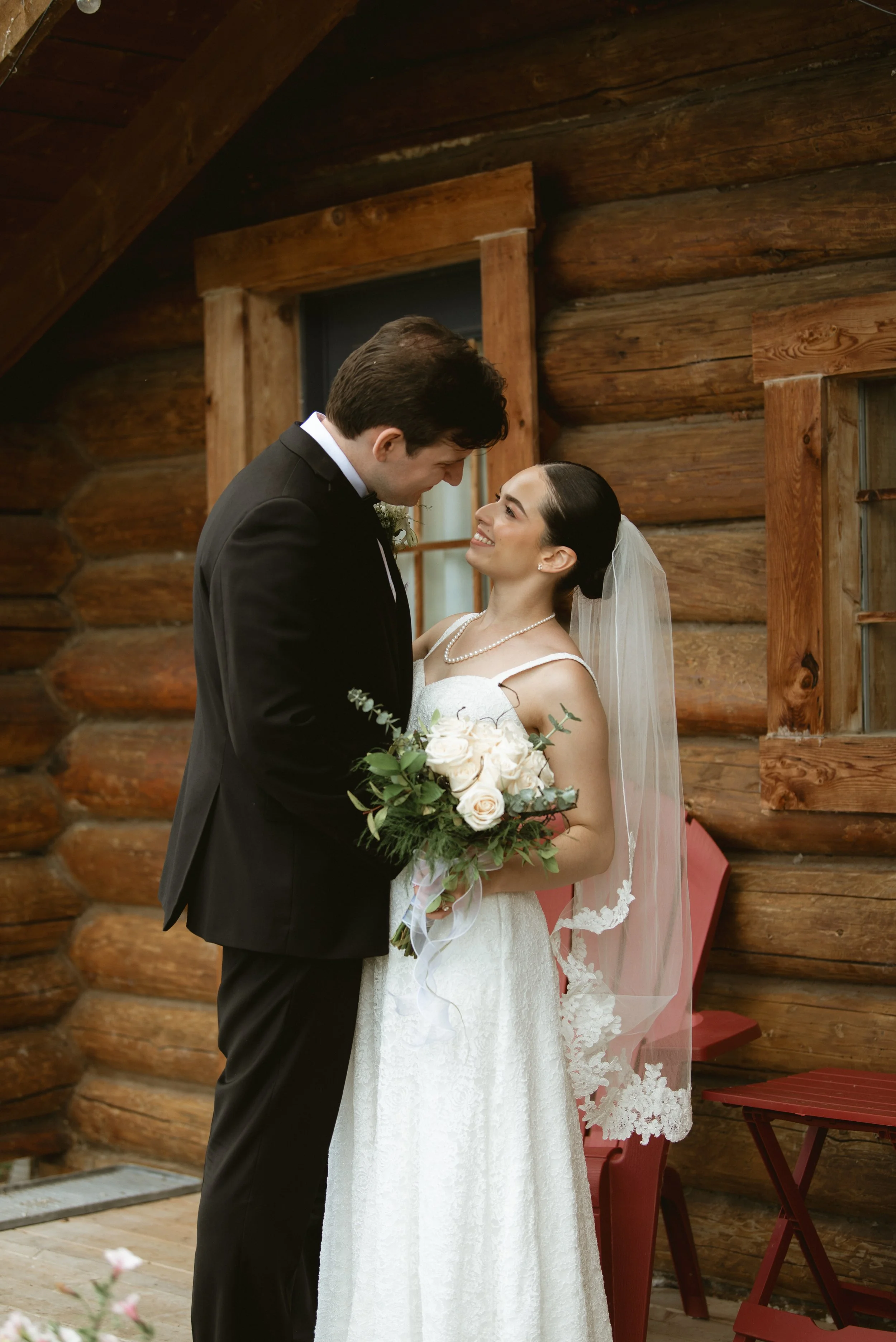 Bride and groom sharing a quiet moment outside the rustic log cabin at Pine & Pond Wedding Venue in Ponoka County, Alberta, photographed by Danielle Aichelle Photography