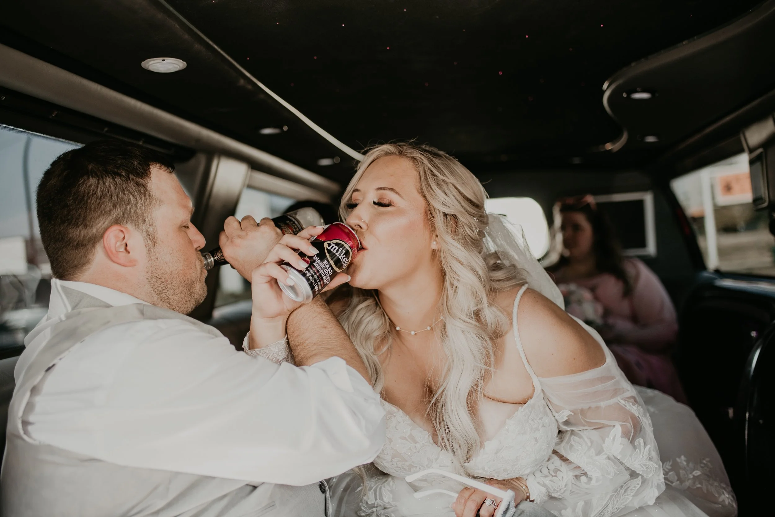 Bride taking a playful drink while sitting with groom during candid wedding moment in Red deer