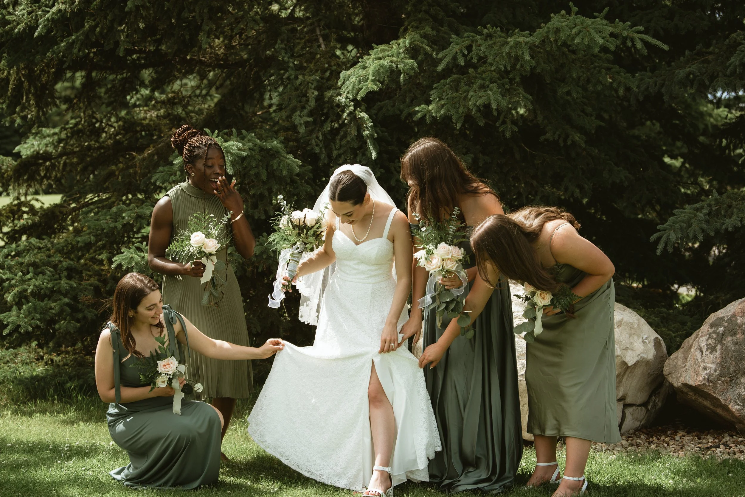 Bridesmaids helping the bride adjust her wedding dress before portraits at Pine & Pond Wedding Venue in Ponoka County, Alberta, photographed by Danielle Aichelle Photography