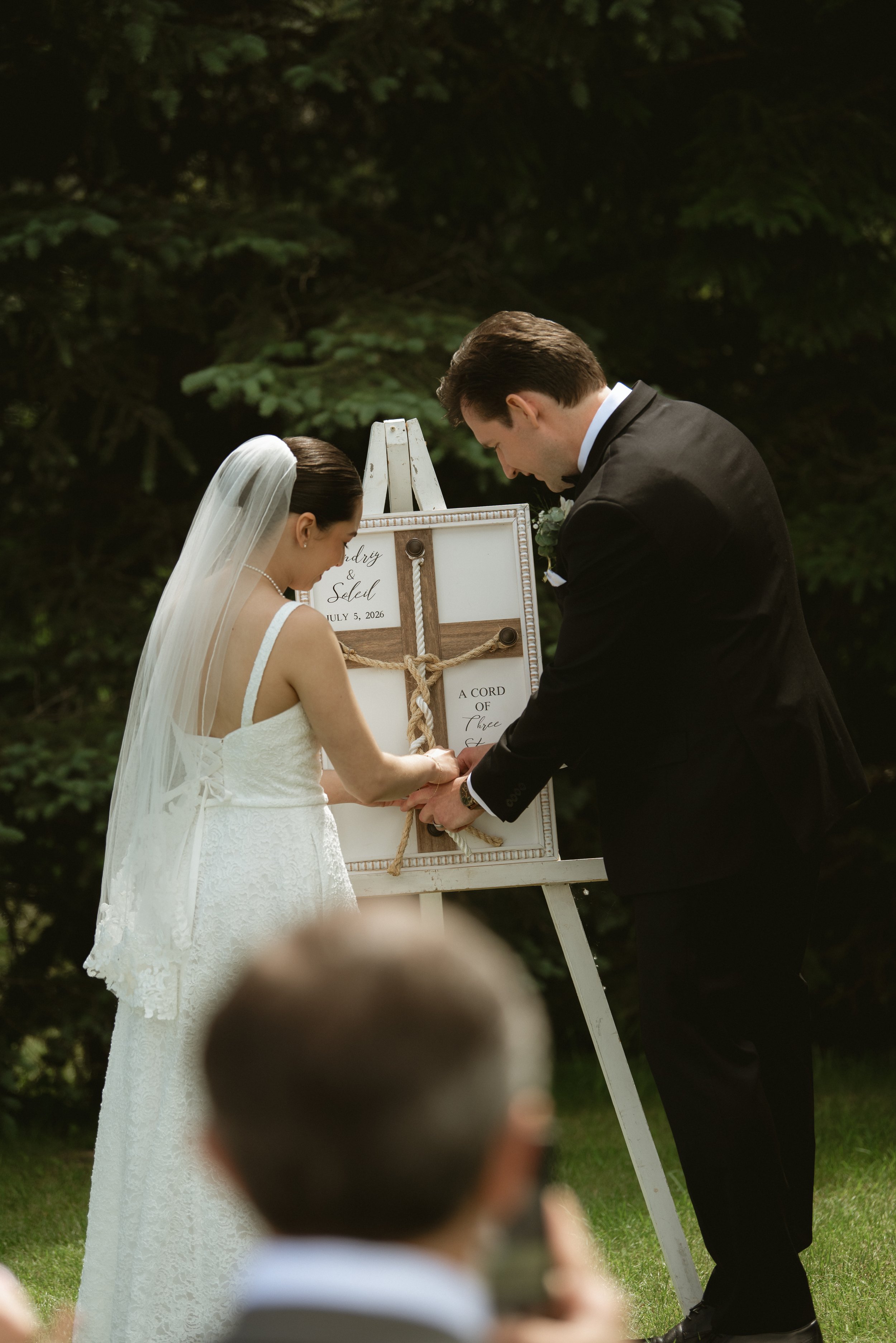 Bride and groom taking part in a cord of three strands unity ceremony during their outdoor wedding at Pine & Pond Wedding Venue in Ponoka County, Alberta, photographed by Danielle Aichelle Photography