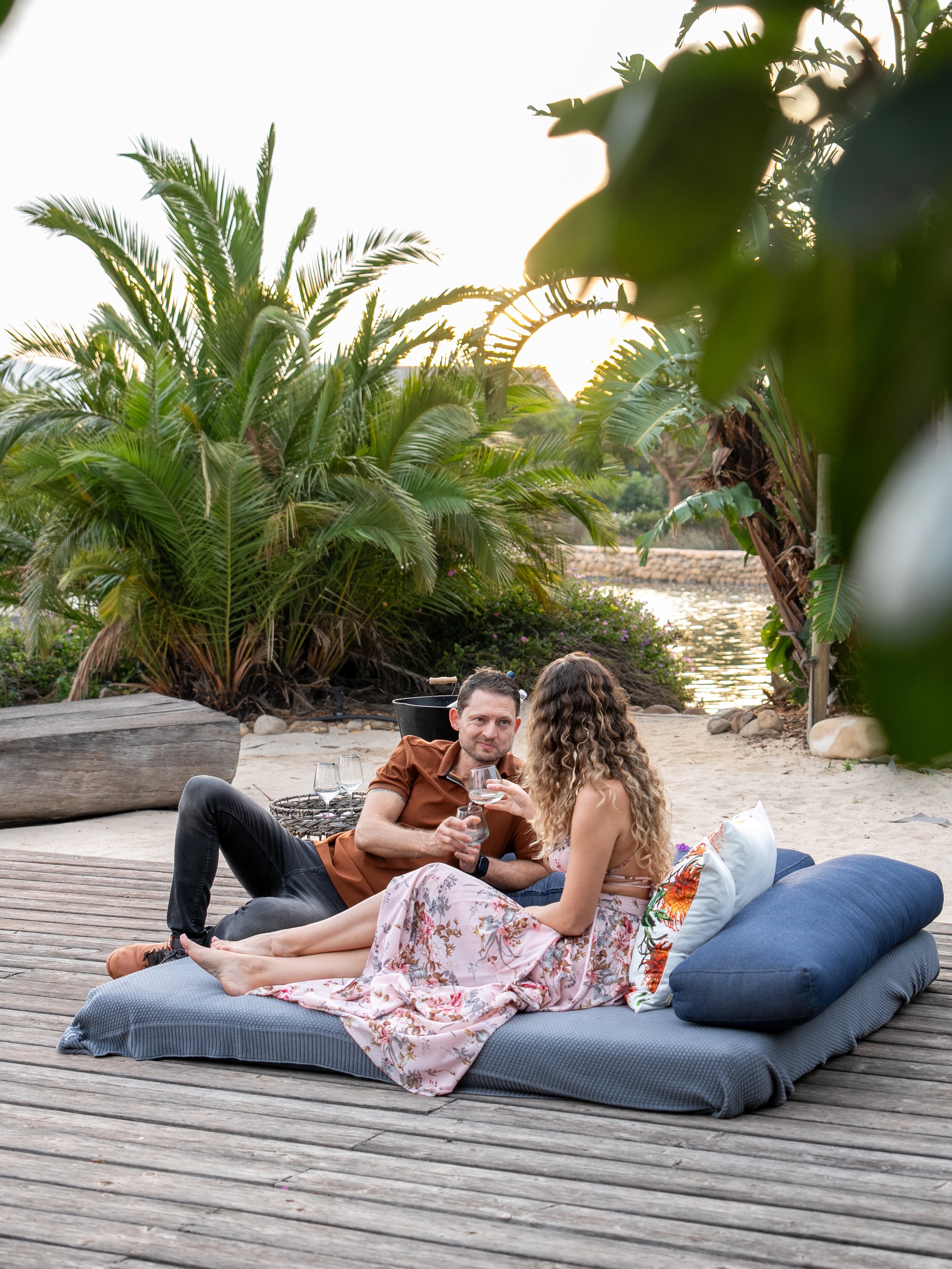Guests relaxing beside the freshwater dam at Ludus Magnus, surrounded by lush greenery and mountain views in the Franschhoek Winelands.