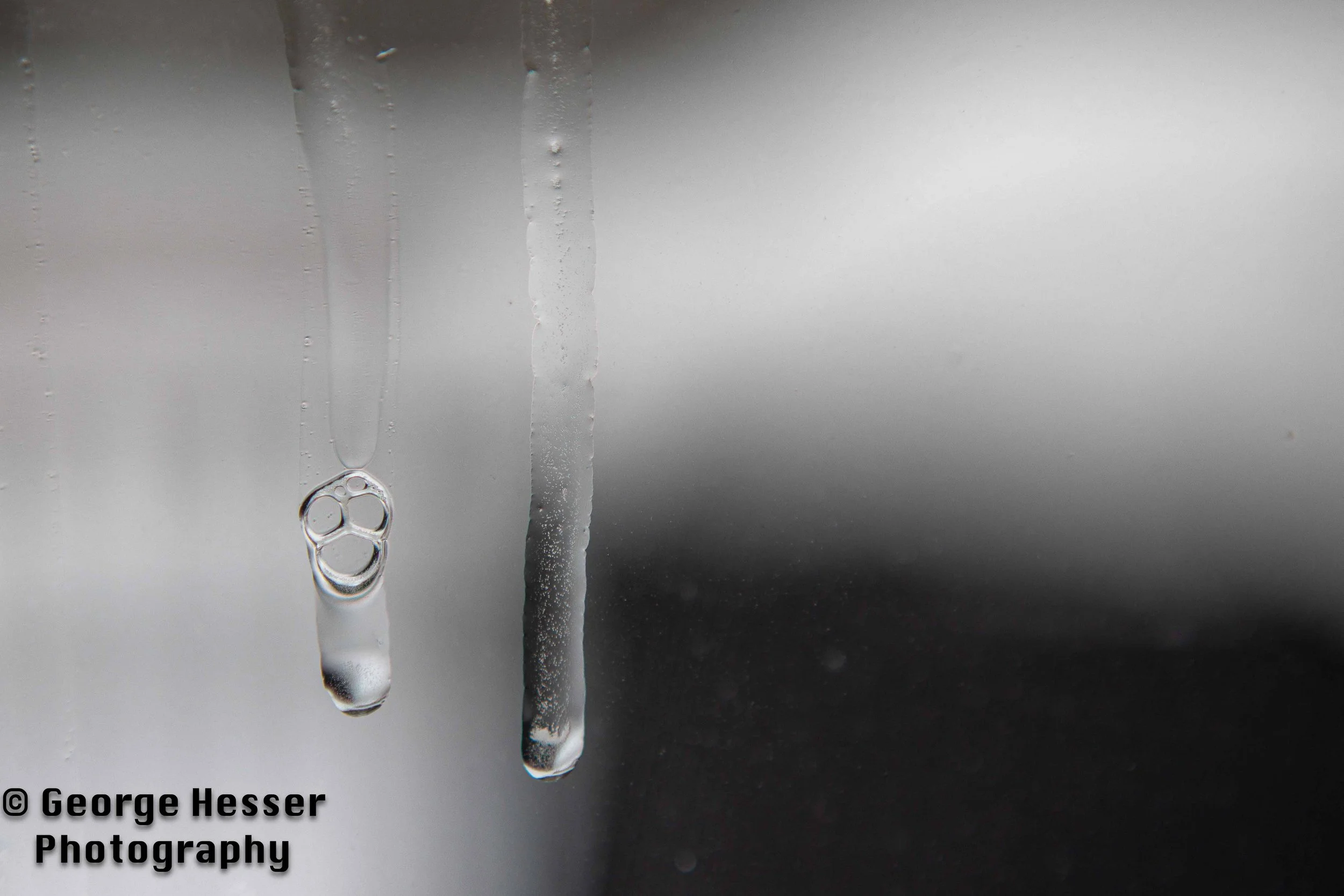 Close-up of two icicles against a blurred background, with visible water droplets inside one icicle.