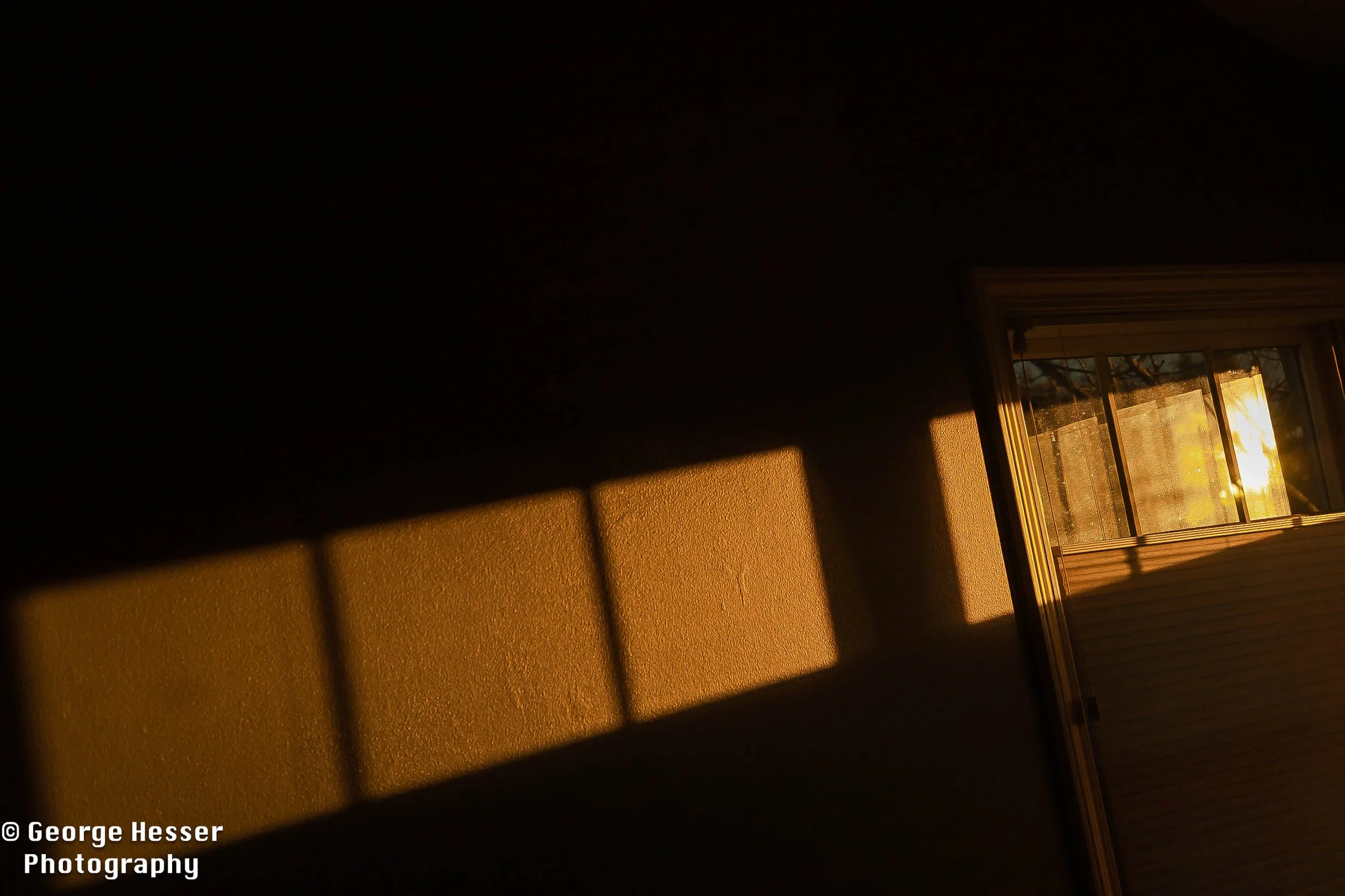 Sunlight and shadows through a window casting rectangles on a dark wall in a room.