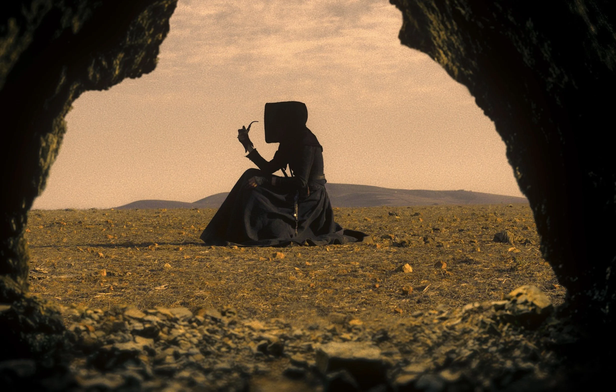 Cloaked woman sat in desert with pipe in Breathing In (2023) review
