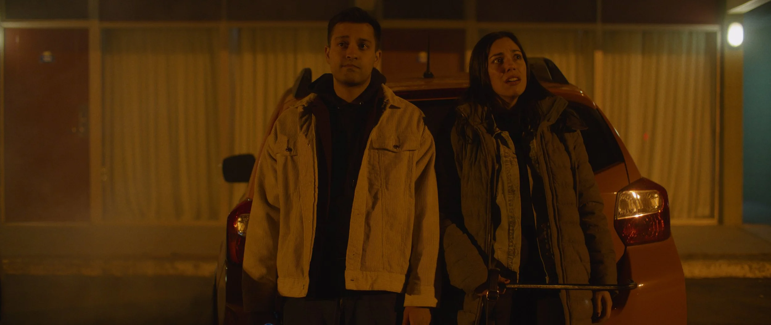 Rian (Rushabh Patel) and Katie (Stephanie Gomes Hogan) stand outside of the Claybourne Motell in I KNOW HOW YOU DIE 2026