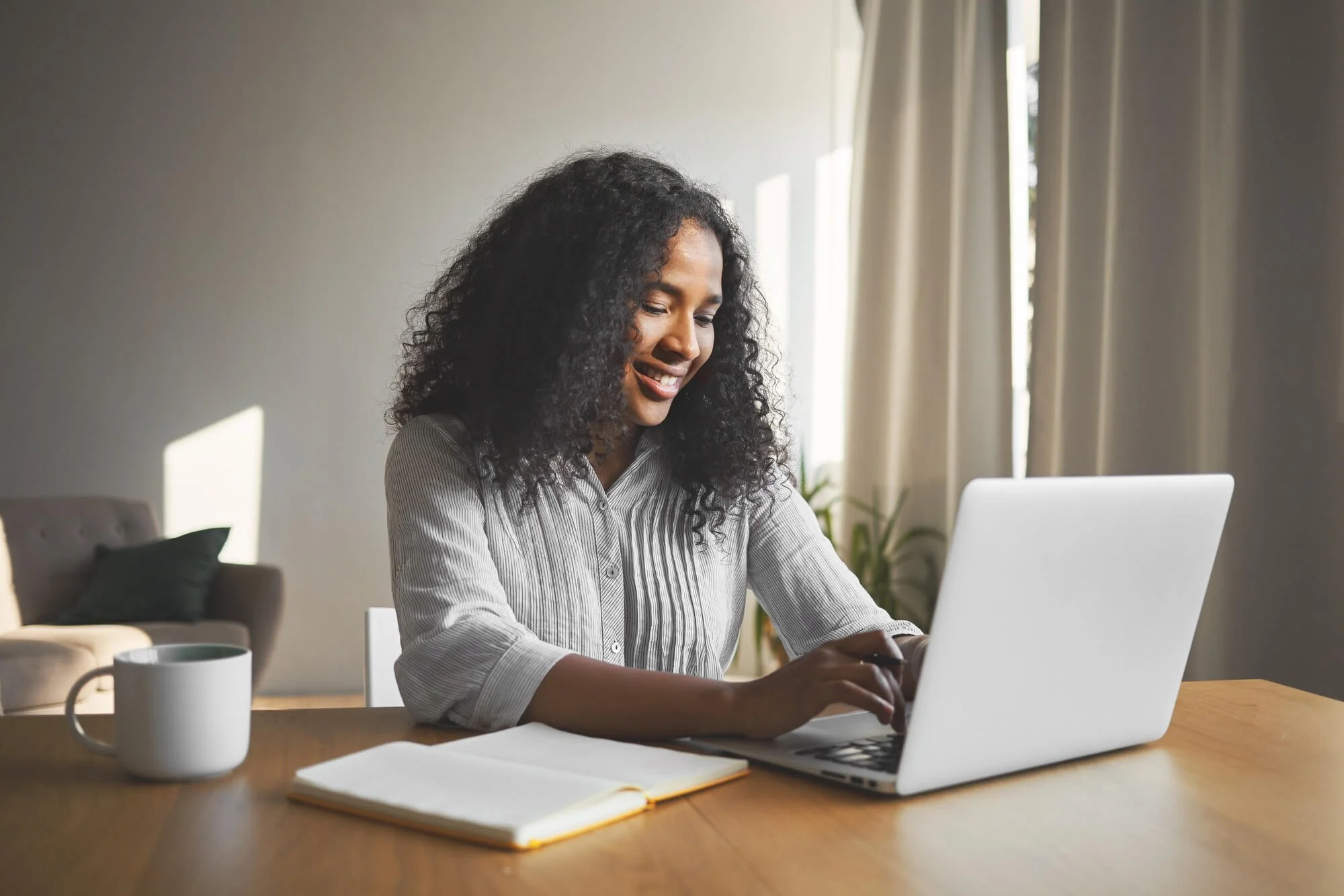 gorgeous-positive-young-dark-skinned-female-blogger-keyboarding-generic-laptop-smiling-being-inspired-while-creating-new-content-her-travel-blog-sitting-desk-with-diary-mug (1).jpg