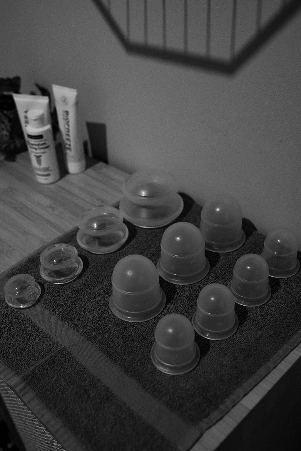 A collection of small, round plastic containers with transparent domed lids, arranged on a textured black mat on a wooden surface, with two tubes of skincare or cosmetic products in the background.