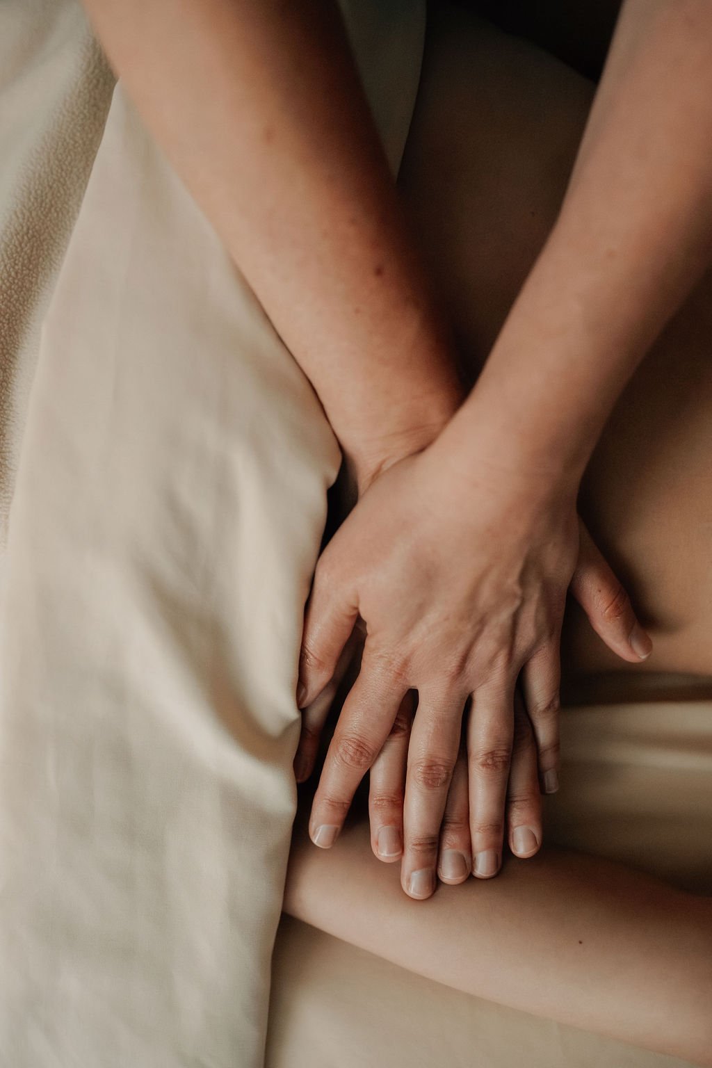 Close-up of a person's hand resting on their leg, with the background showing a beige pillow and bed sheet.