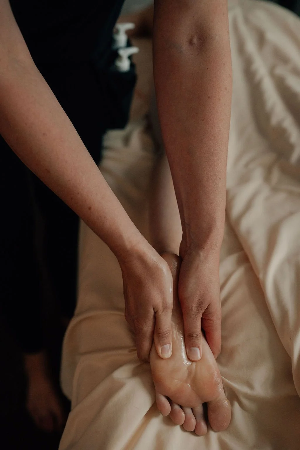 Person receiving a foot massage or foot care, with hands holding and massaging a foot over a cream or lotion on the skin.