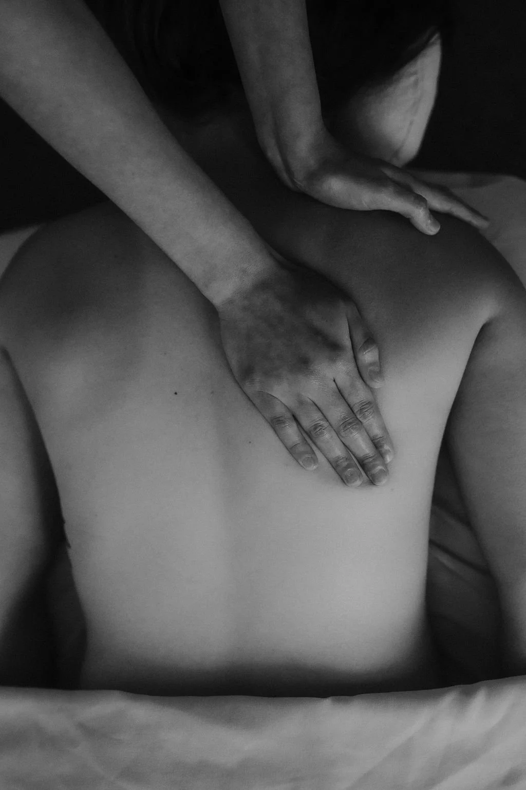 A person receiving a massage on their back with a massage therapist's hands pressing down on their shoulder and upper back.