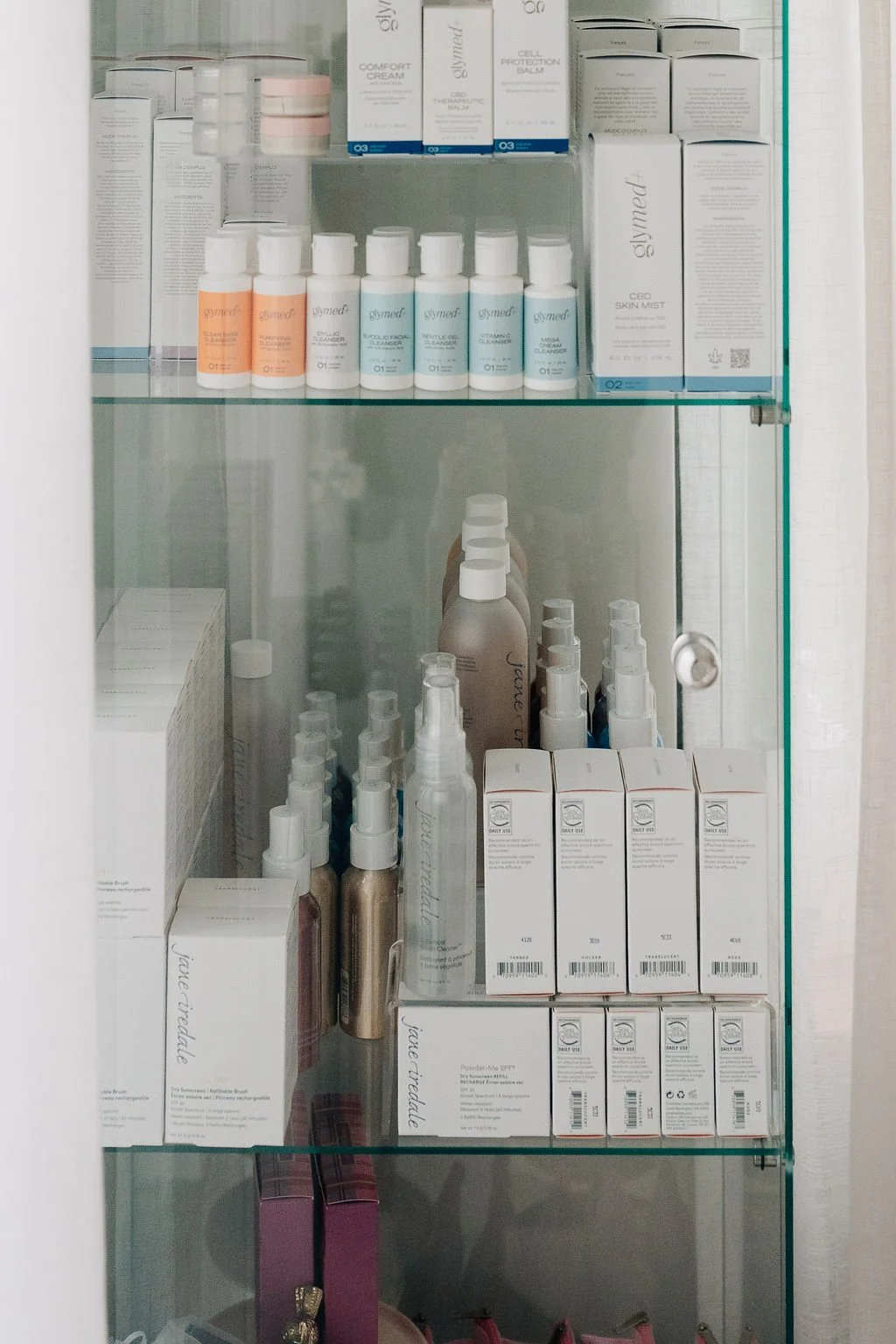 A glass shelf containing skincare and beauty products, including sprays, creams, and serums, organized in rows.